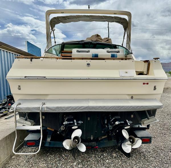 1987 Sea Ray 270 Sundancer boat, rear view with dual propellers, parked on gravel.