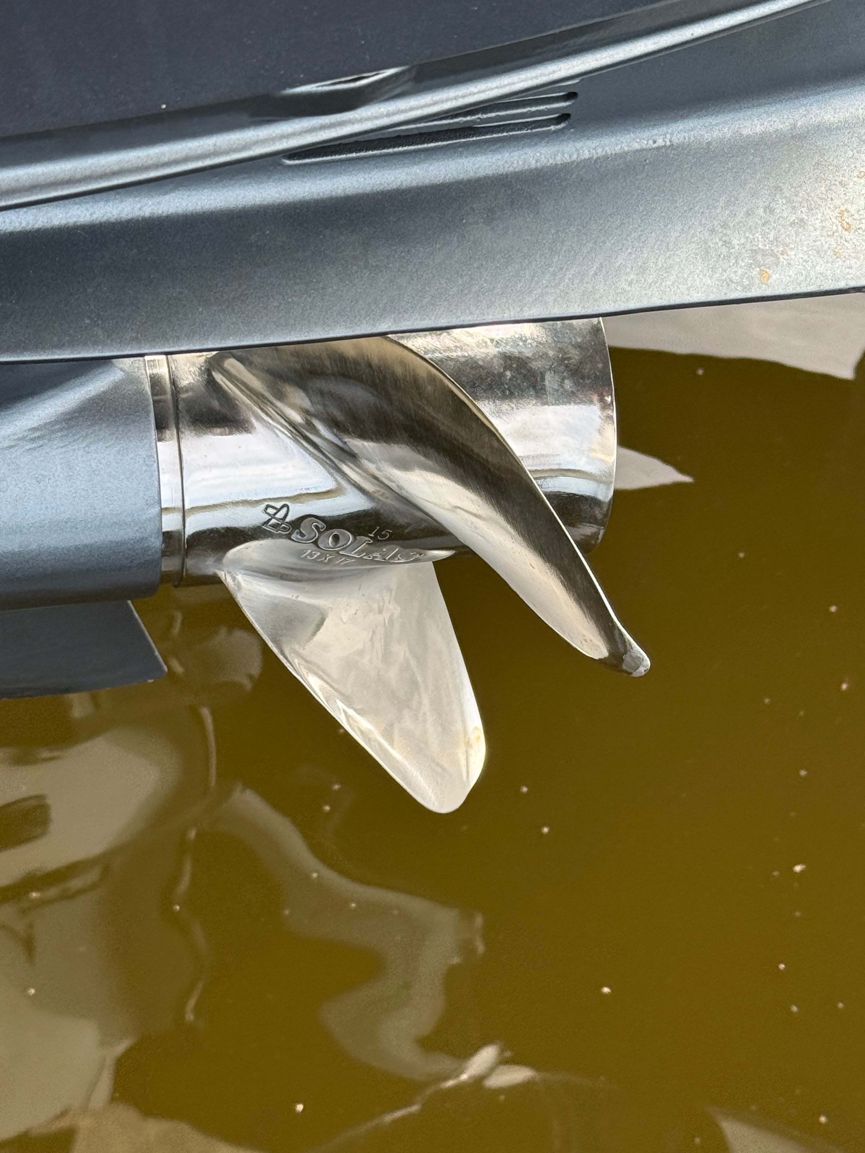 Close-up of a shiny boat propeller above calm water.