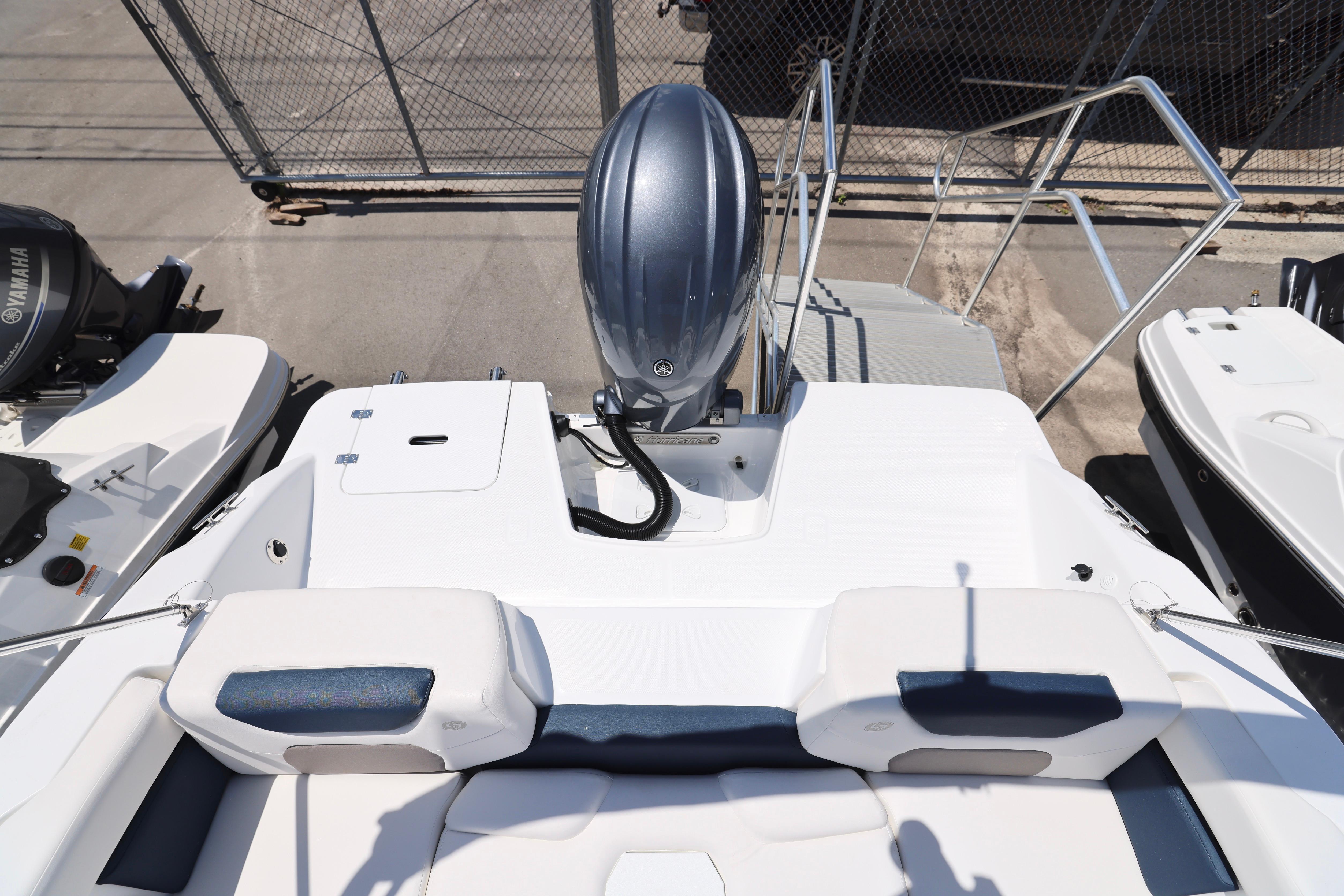 2026 Hurricane SunDeck 2050 OB boat with outboard motor, docked near a fence.