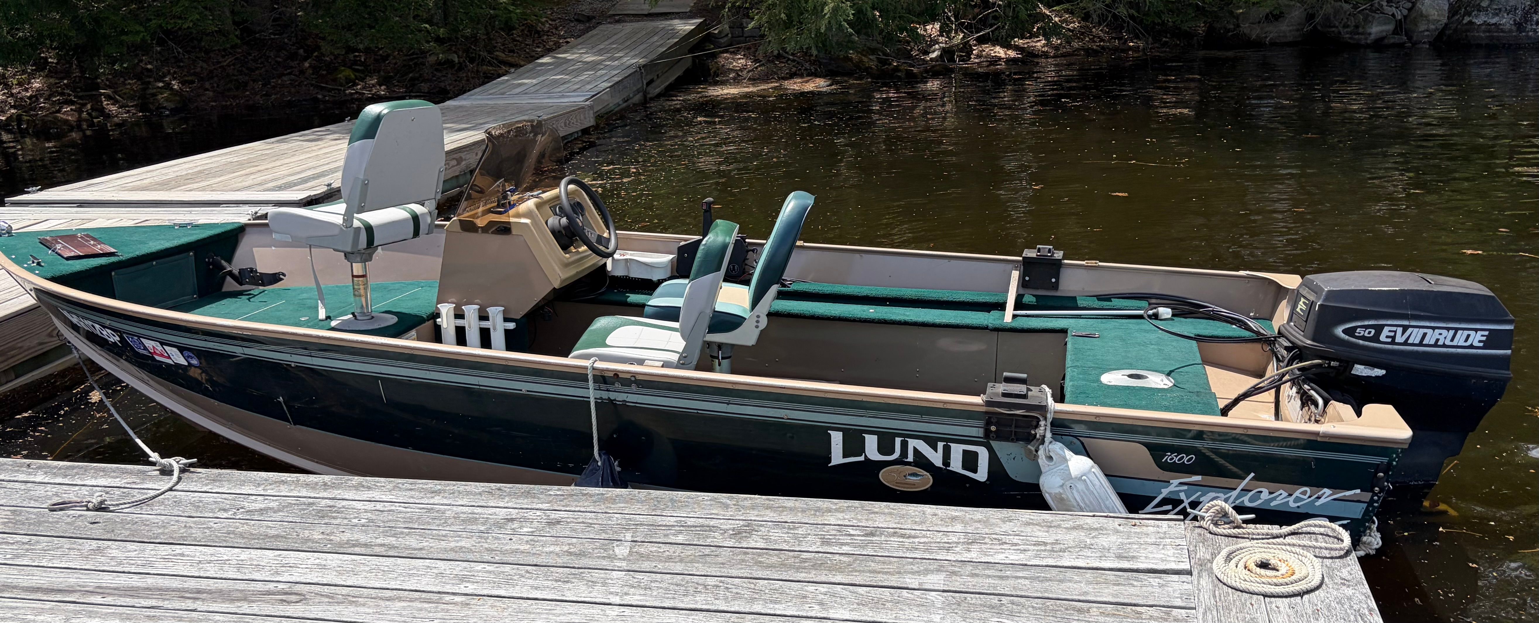 A 1998 Lund Explorer SS boat docked at a wooden pier. It features green seats and an outboard motor.