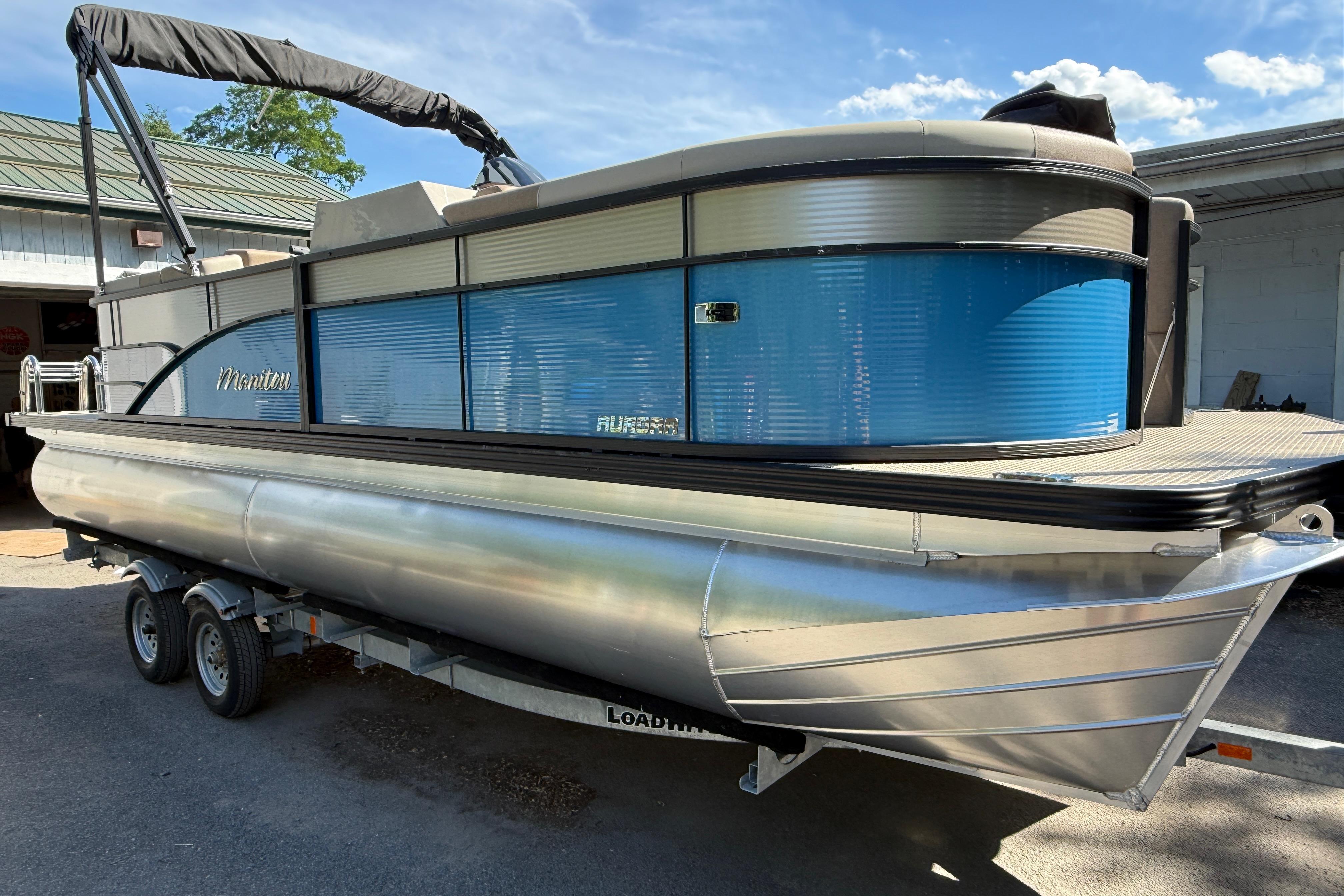 2027 Manitou Aurora RF 23 pontoon boat on trailer, featuring sleek blue and silver design.