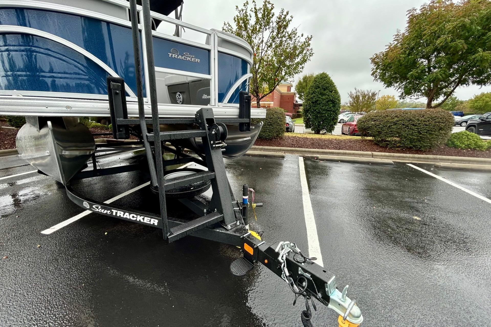 2026 Sun Tracker SportFish 22 DLX pontoon boat on trailer in parking lot.