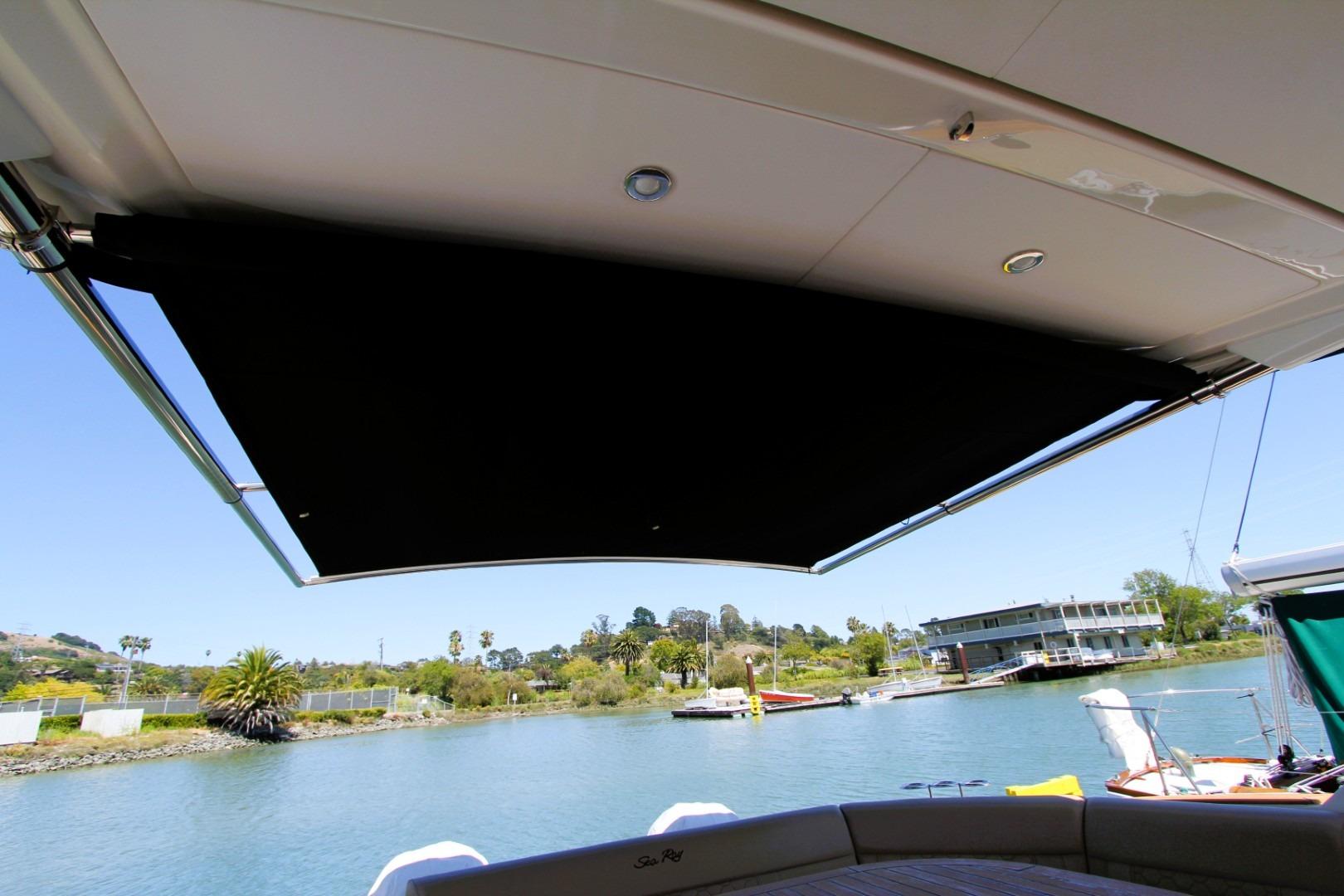 2021 Sea Ray Sundancer 320 Outboard with extended sunshade on a serene waterfront.