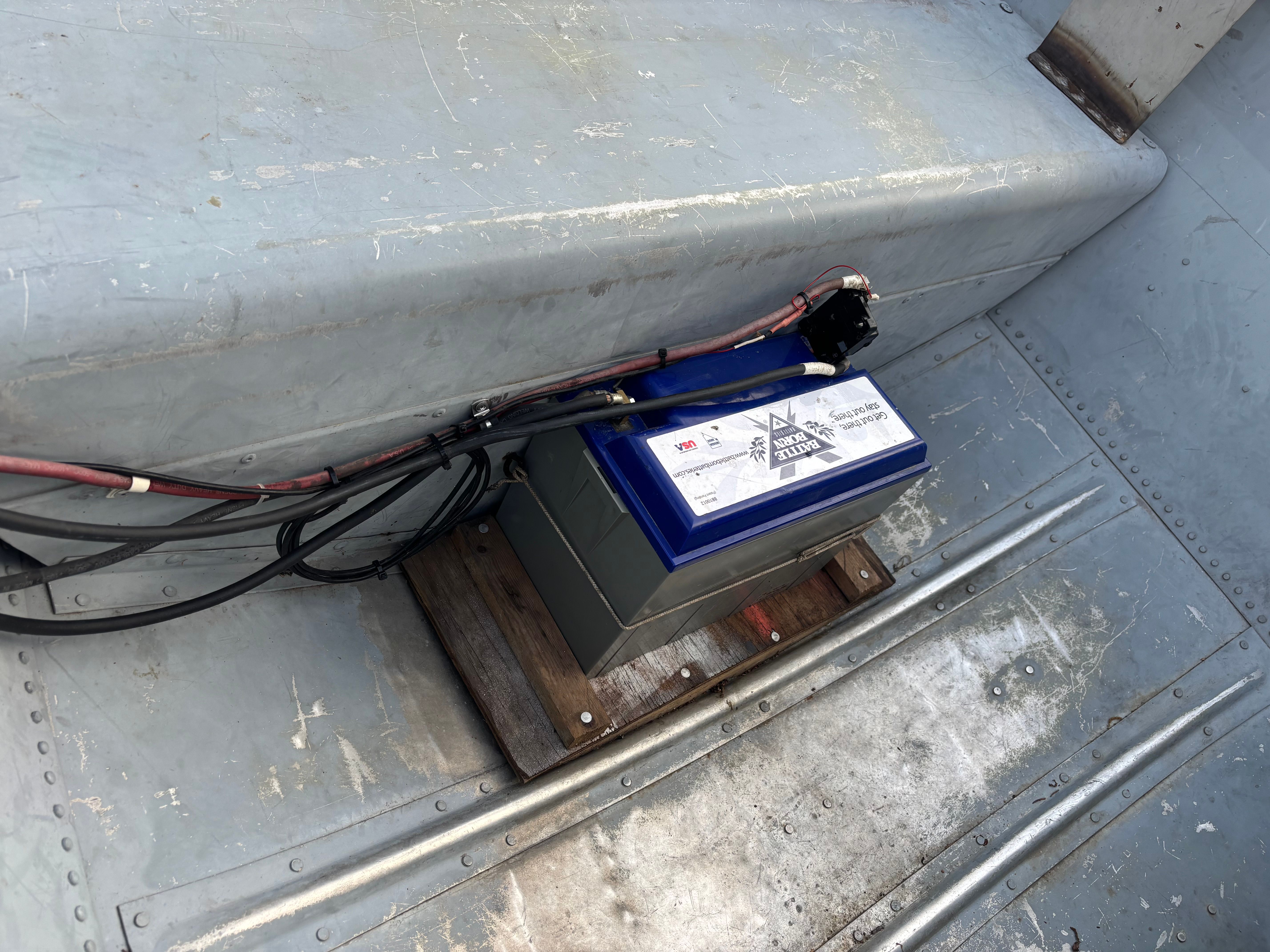 A boat battery is mounted on the floor of a gray boat.