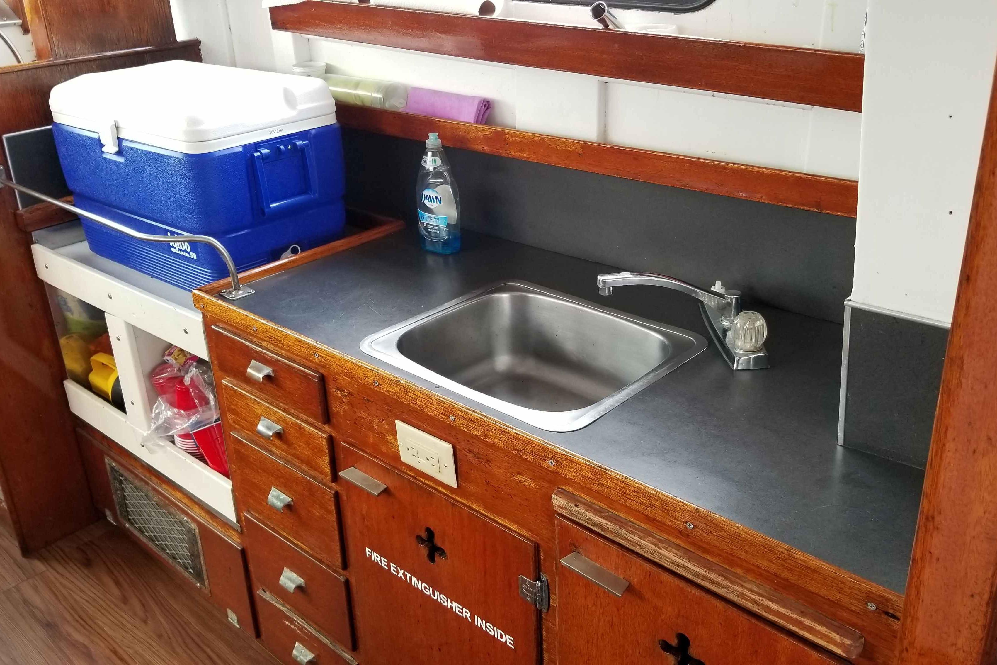 1964 Grandy Tour Boat interior with wooden cabinetry, sink, and cooler.