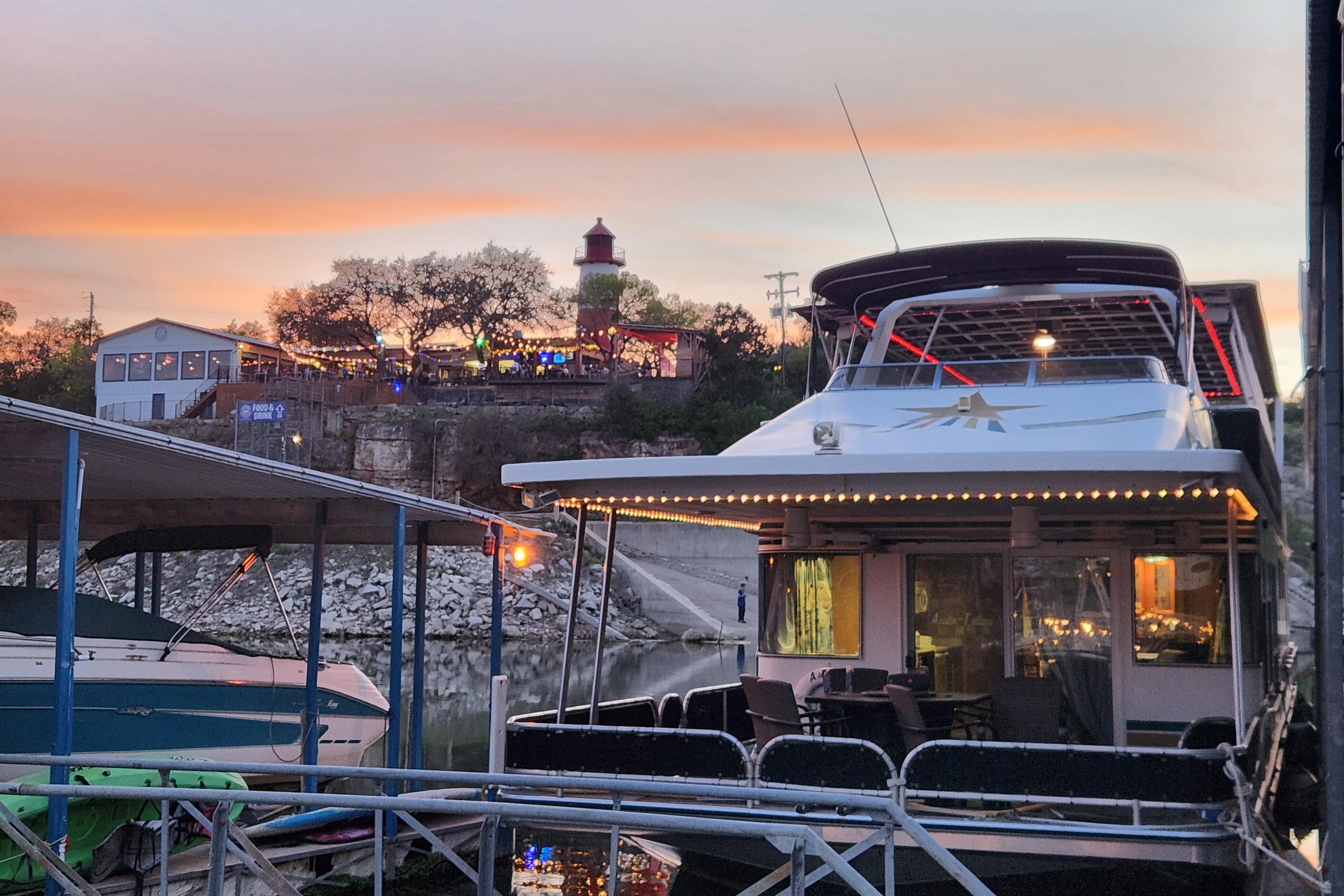 Houseboat docked at sunset near a lively waterfront area, featuring a Sharpe 85 model from 2000.
