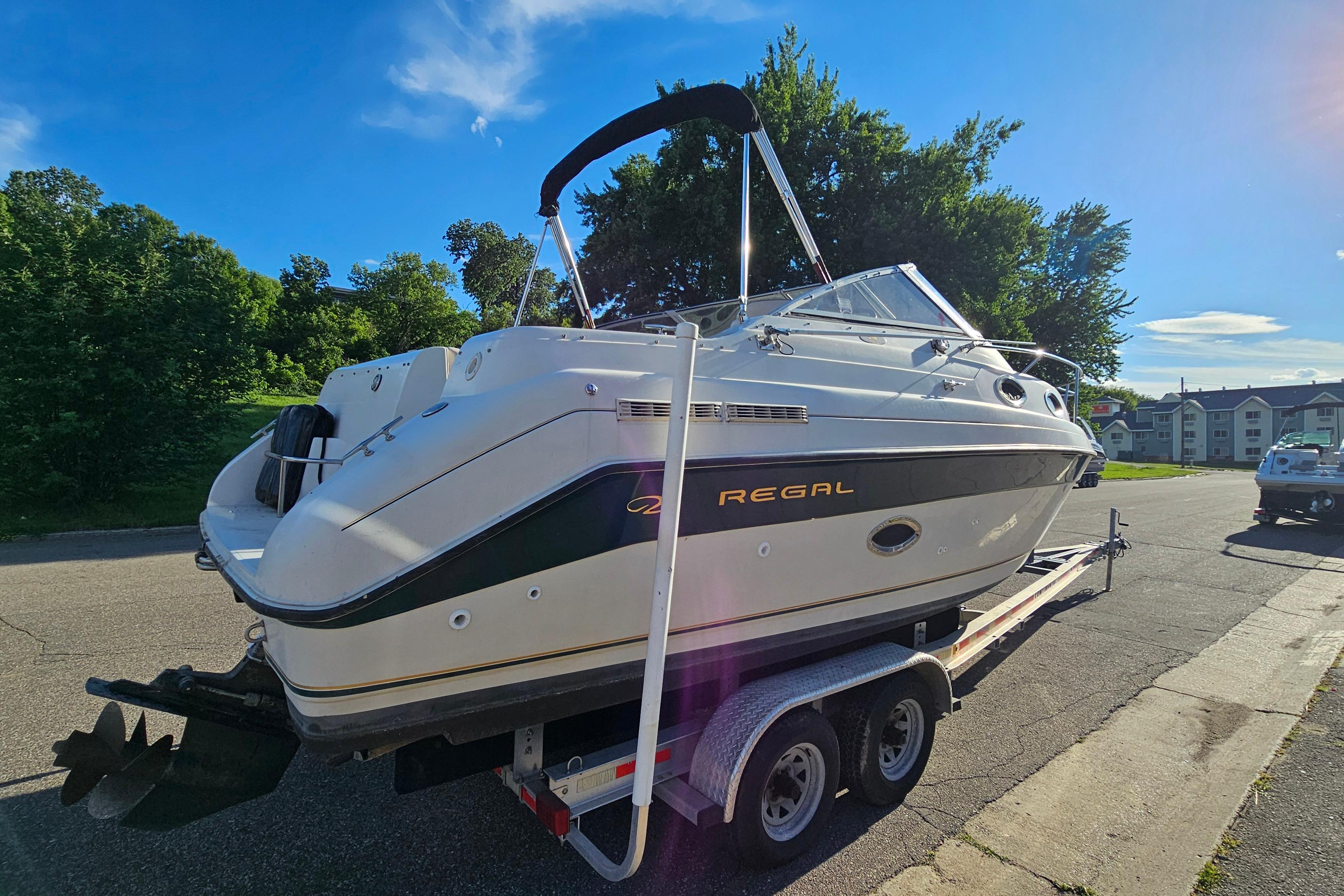 1999 Regal Commodore 258 boat on trailer, parked on a sunny street with trees.