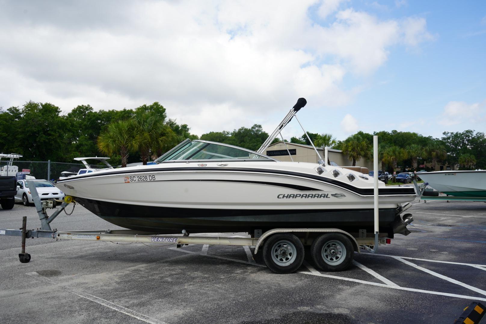 2013 Chaparral 206 SSi boat on trailer in parking lot, surrounded by trees.
