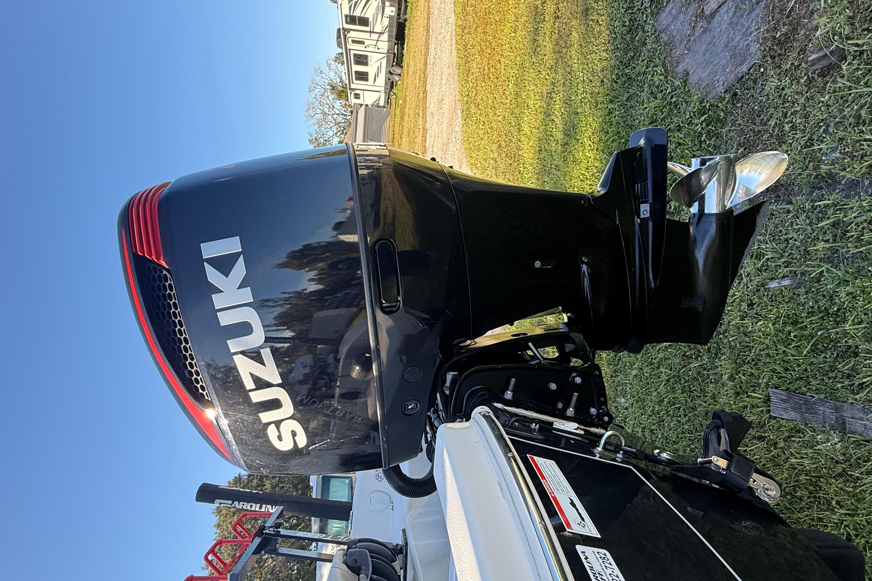 Suzuki outboard motor on 2021 Carolina Skiff 26 Ultra Elite boat, parked on grass.