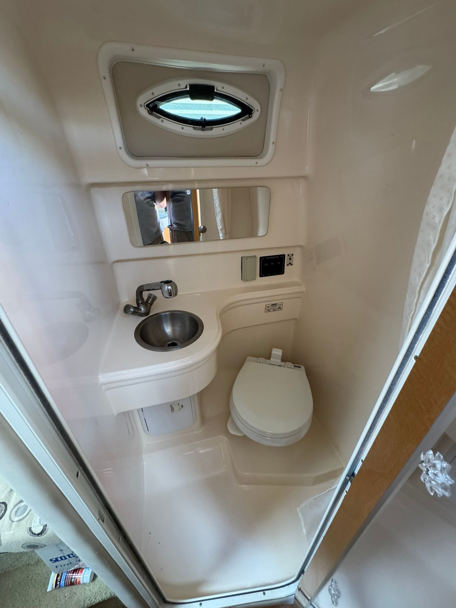 Small bathroom on a boat with a toilet, sink, and mirror.