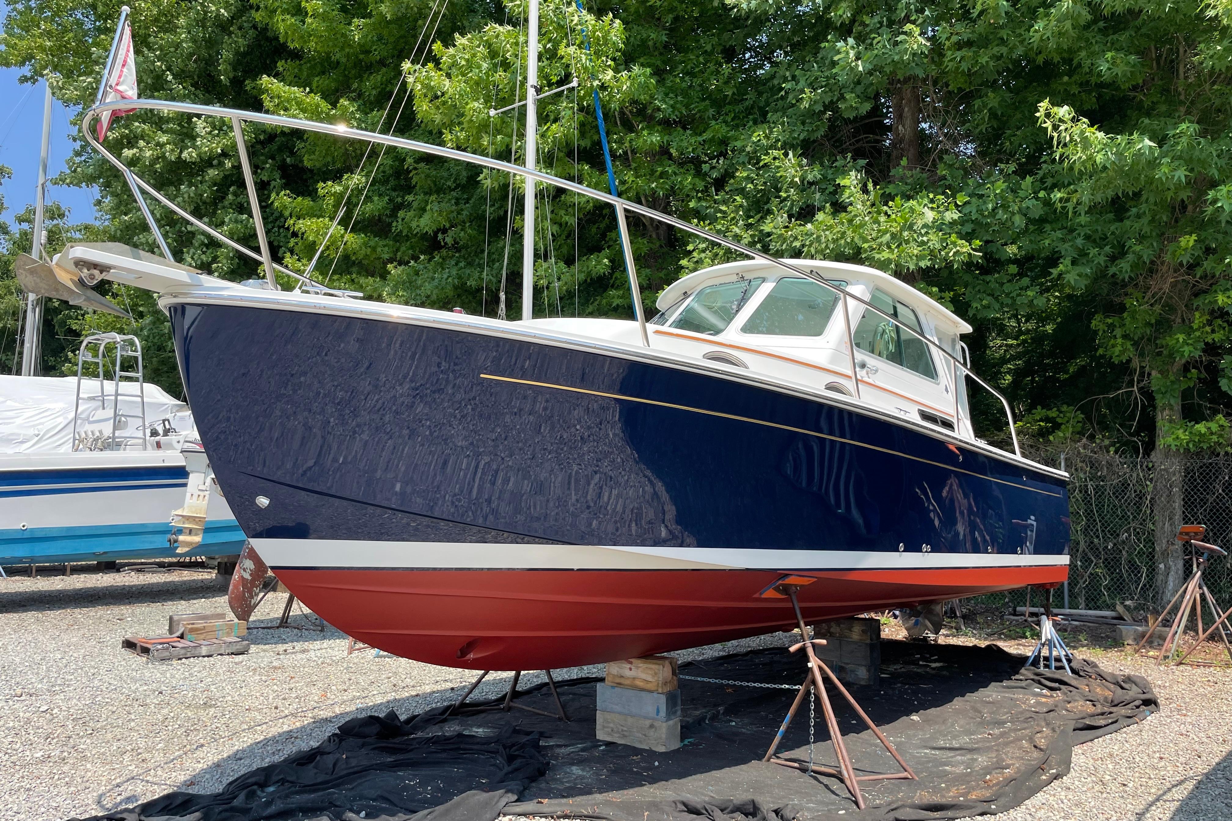 2007 Back Cove 29 boat on stands, blue hull, red bottom, surrounded by trees.