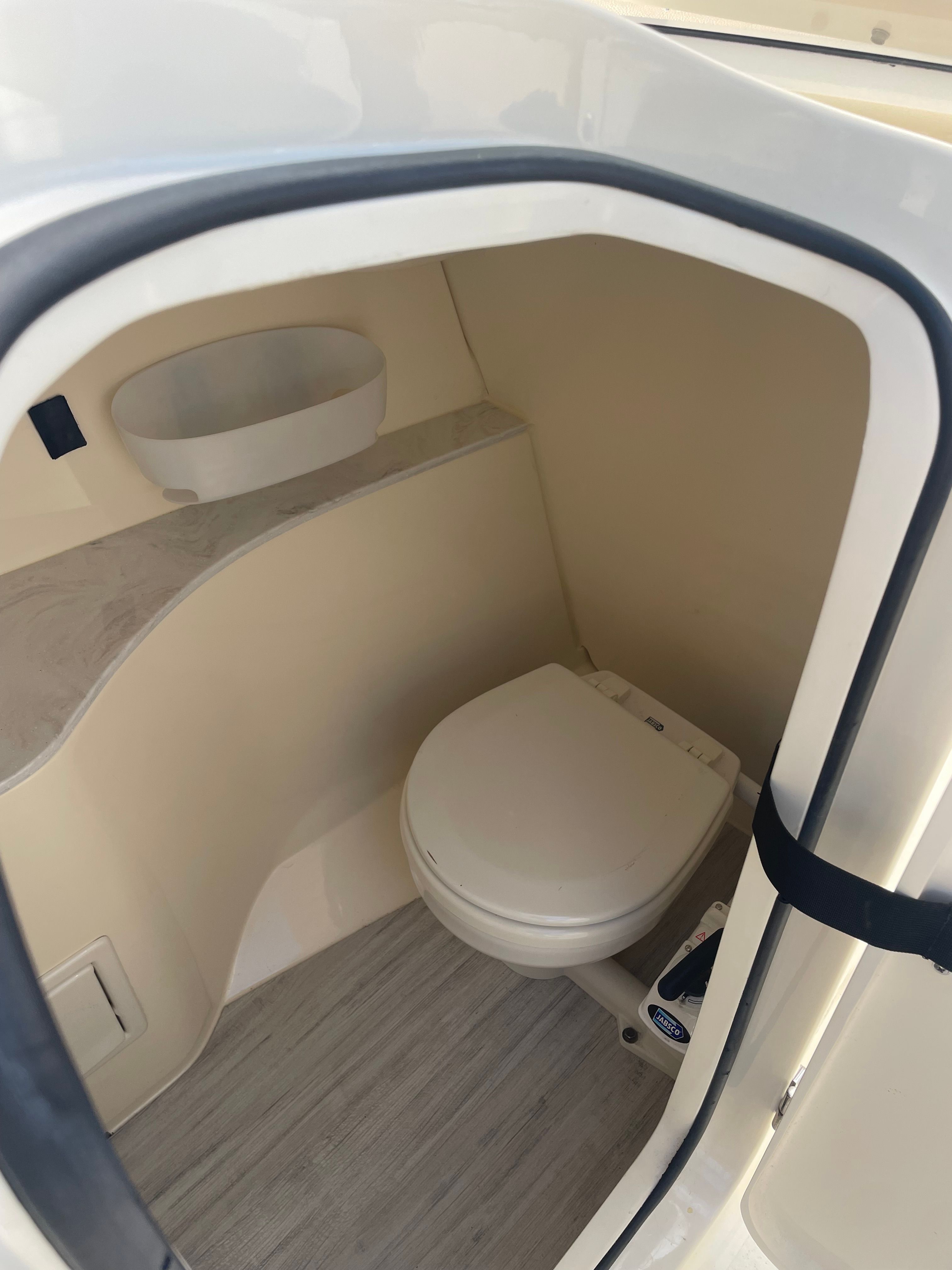 The image shows a compact boat toilet with a white toilet and beige interior.