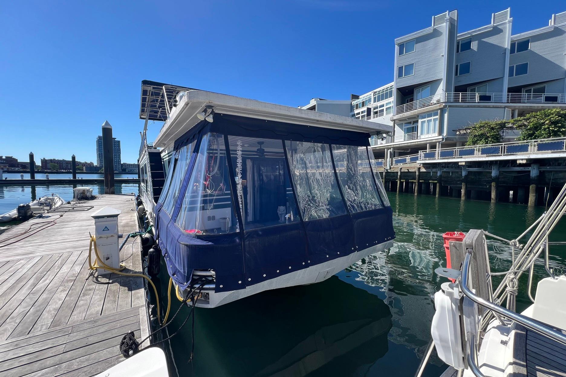 1993 Sumerset houseboat docked at marina, featuring blue canopy and waterfront buildings.