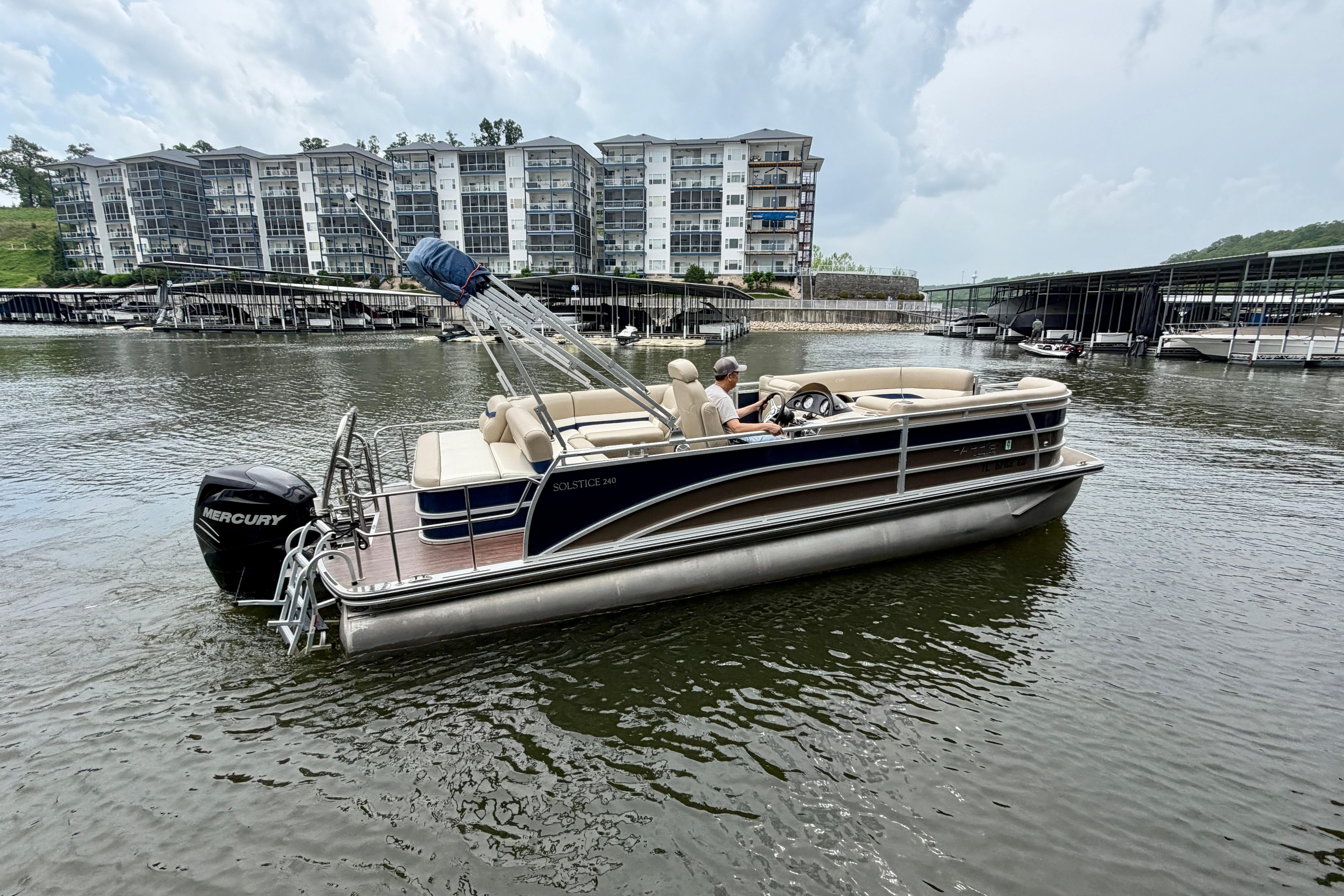 2013 Harris Solstice 240 pontoon boat on a lake near modern apartments.