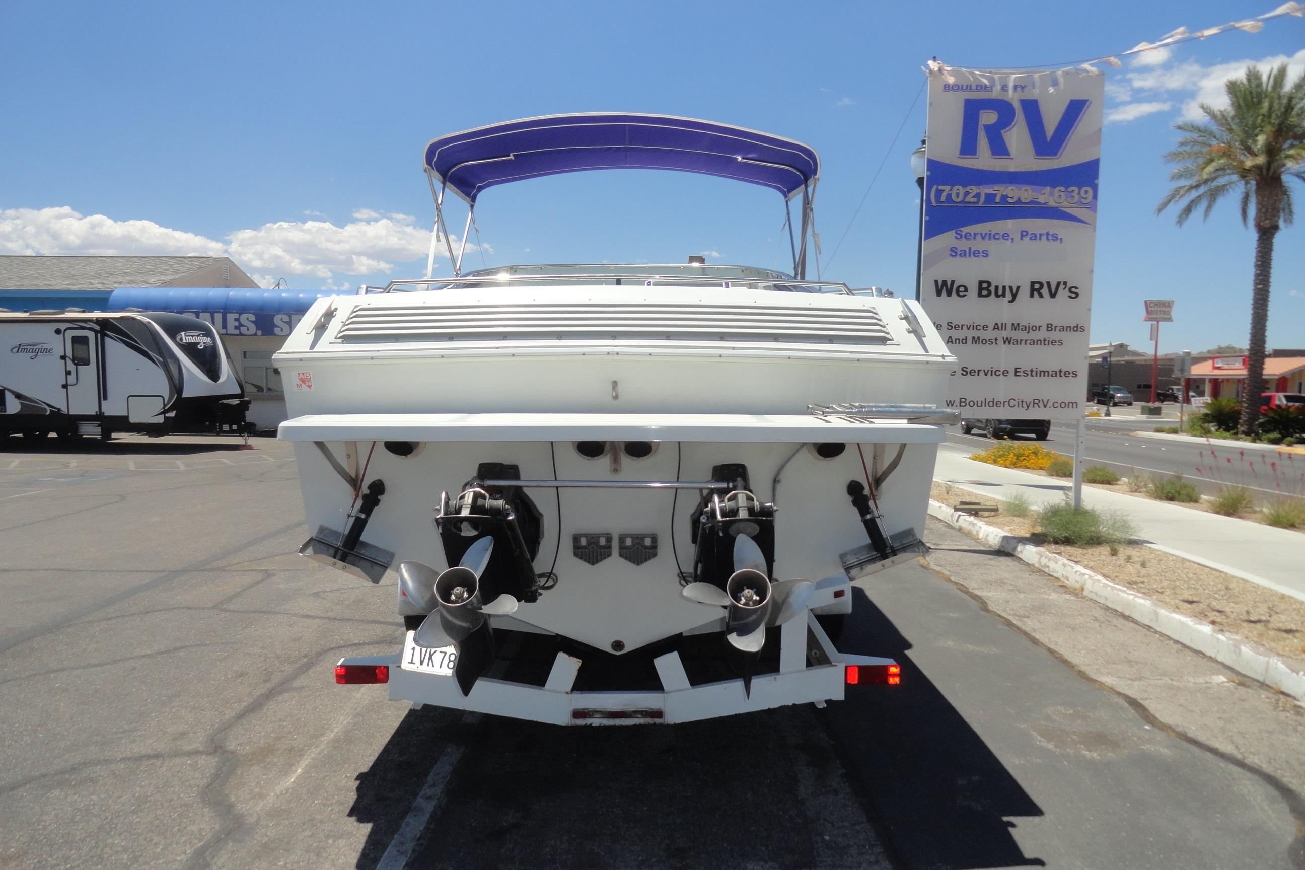 1988 Wellcraft 34 Scarab boat on trailer, parked near RV dealership under clear sky.