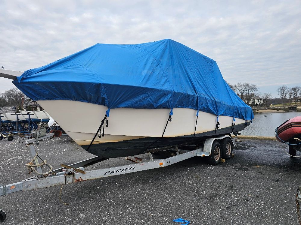 A 1997 Grady-White Chase 263 boat on a trailer, covered with a blue tarp.