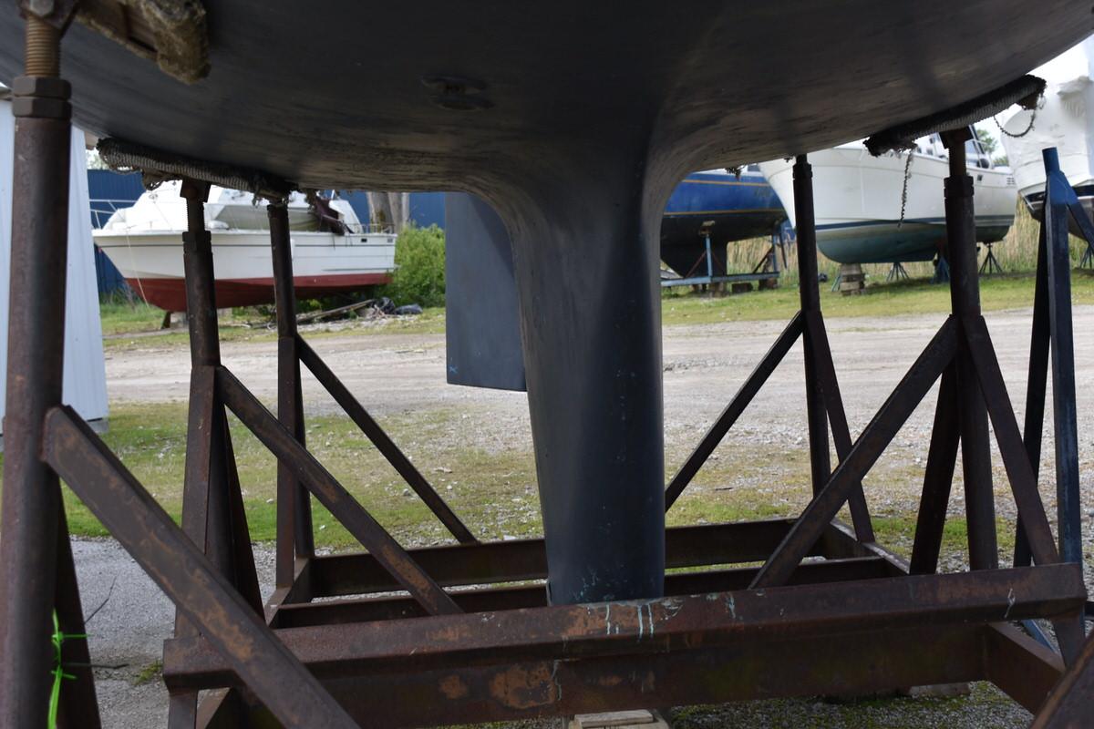 Underside of a sailboat on a stand, with keel visible, surrounded by other boats.