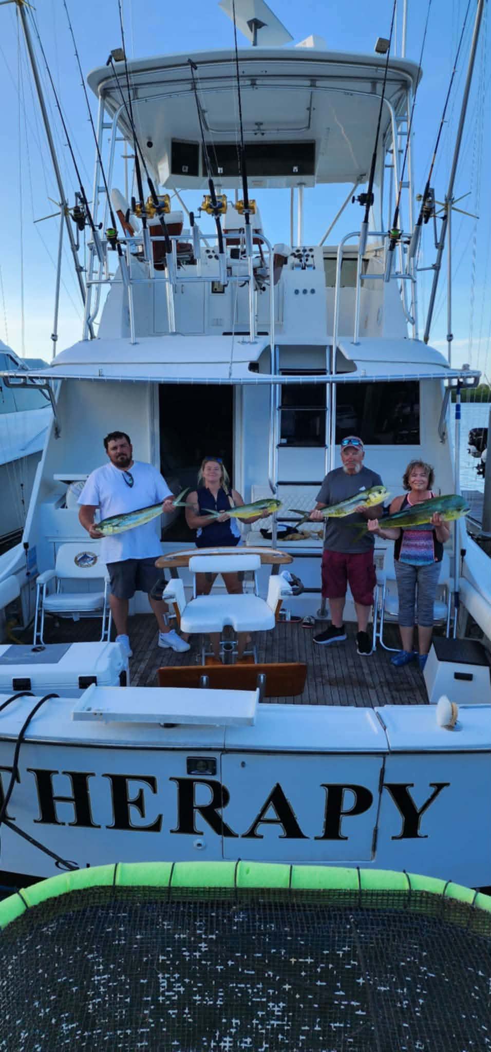 Four people stand on a sport fishing boat holding caught fish.