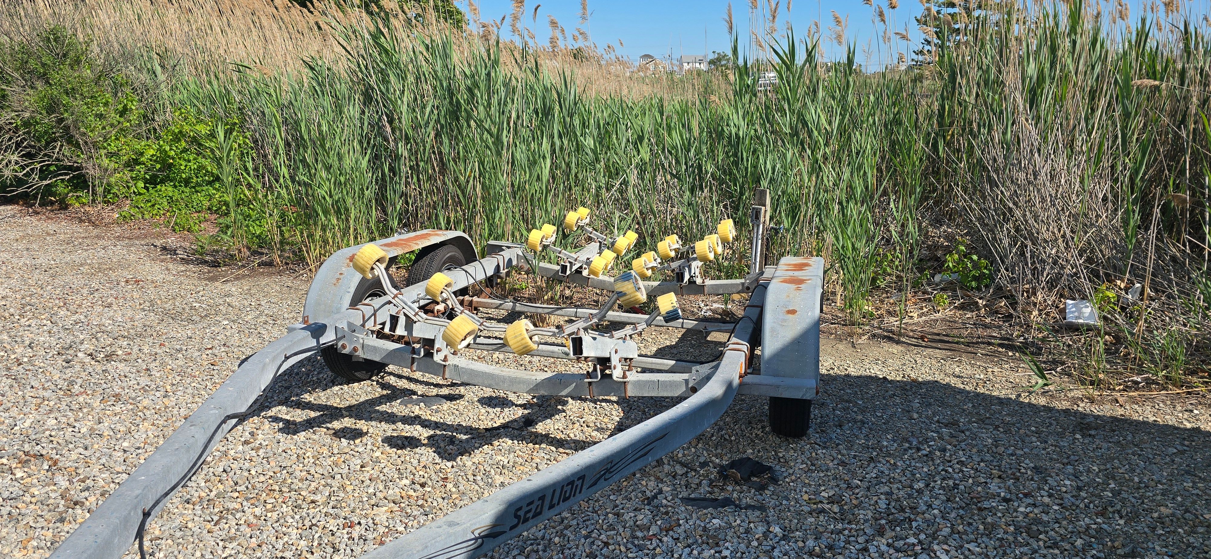 Boat trailer on a gravel path, surrounded by tall grass.