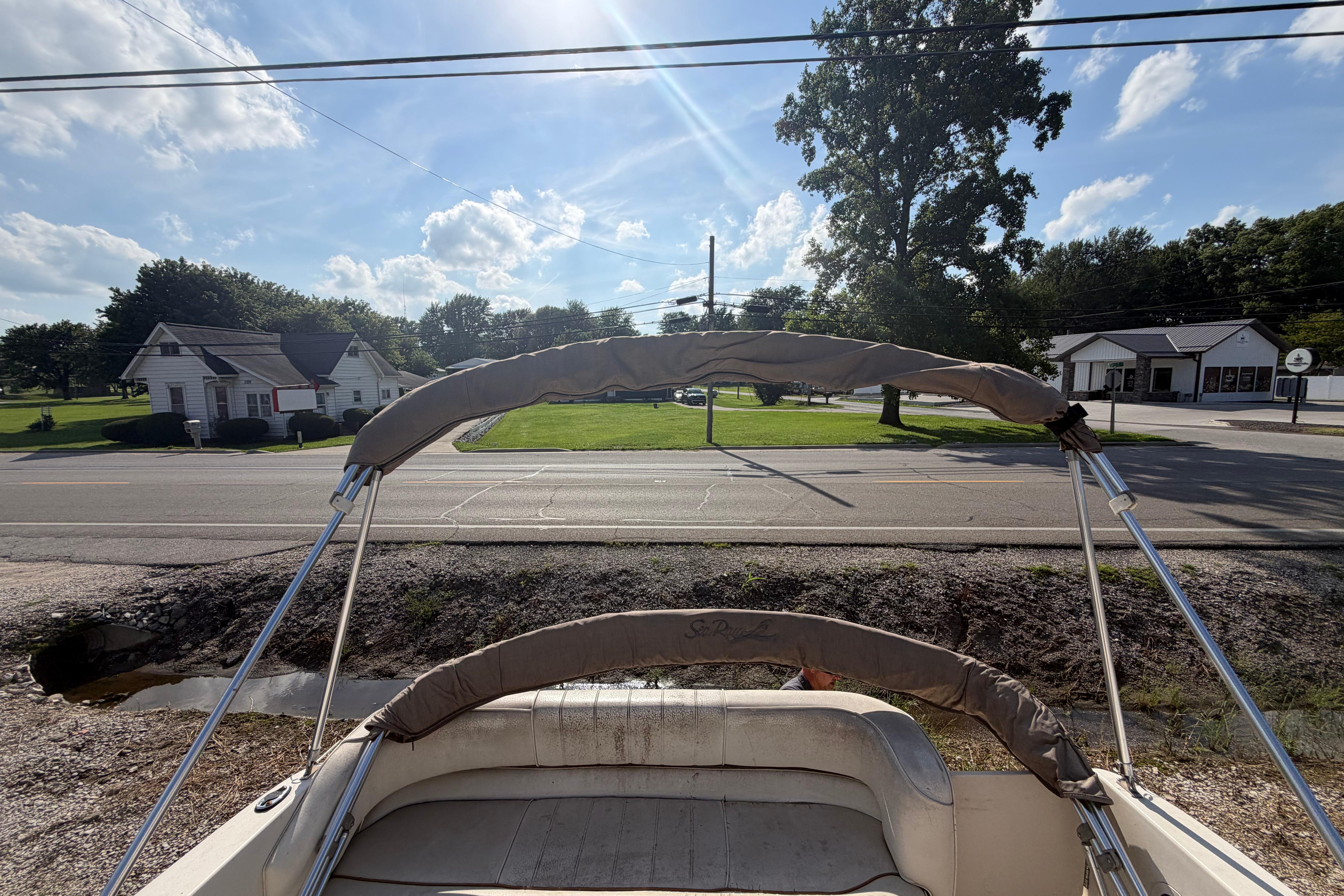 1999 Sea Ray 240 Sundancer boat with bimini top, parked near a road under a sunny sky.