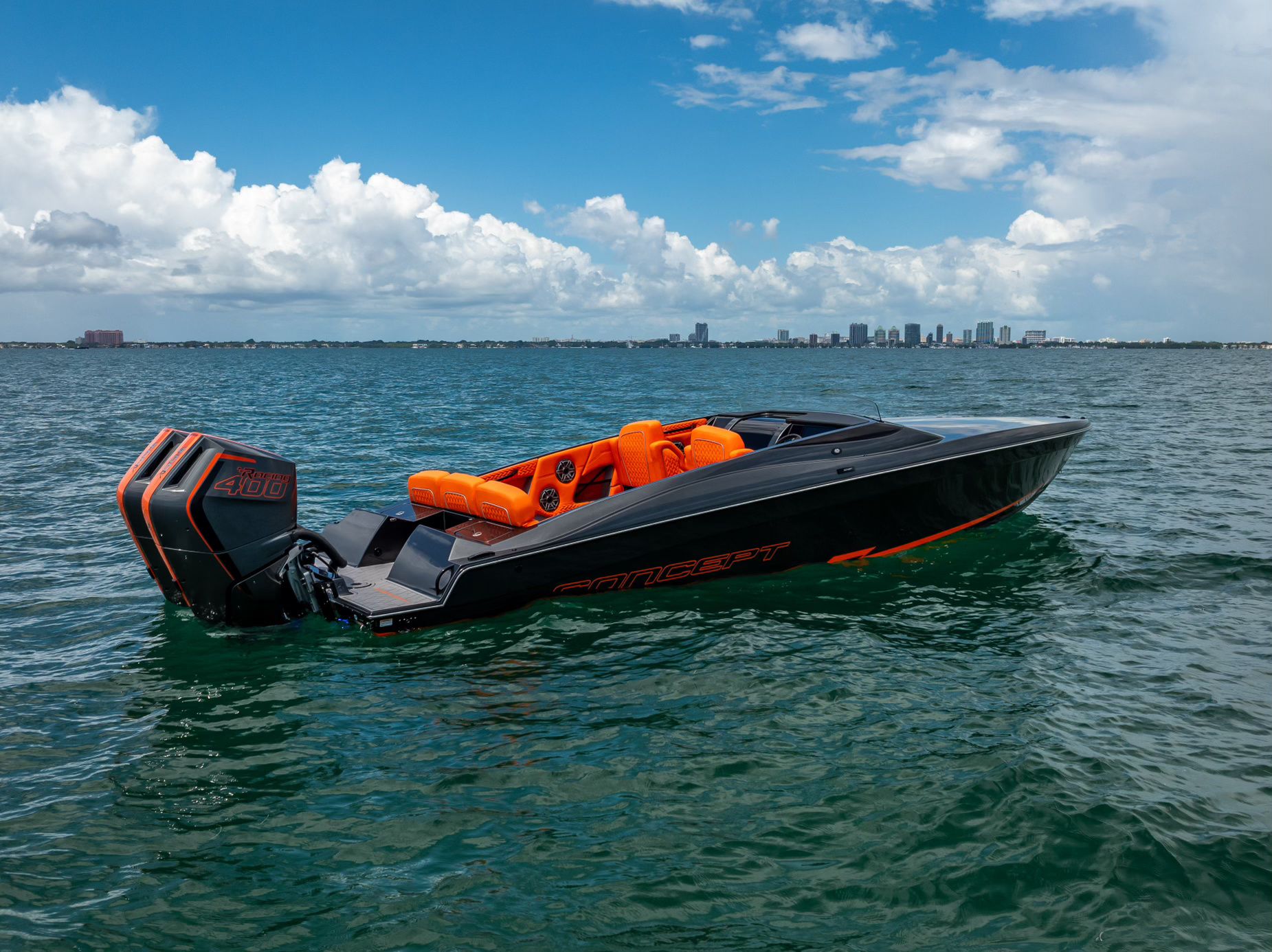 A modern sport boat with bright orange seats on calm water, set against a city skyline.