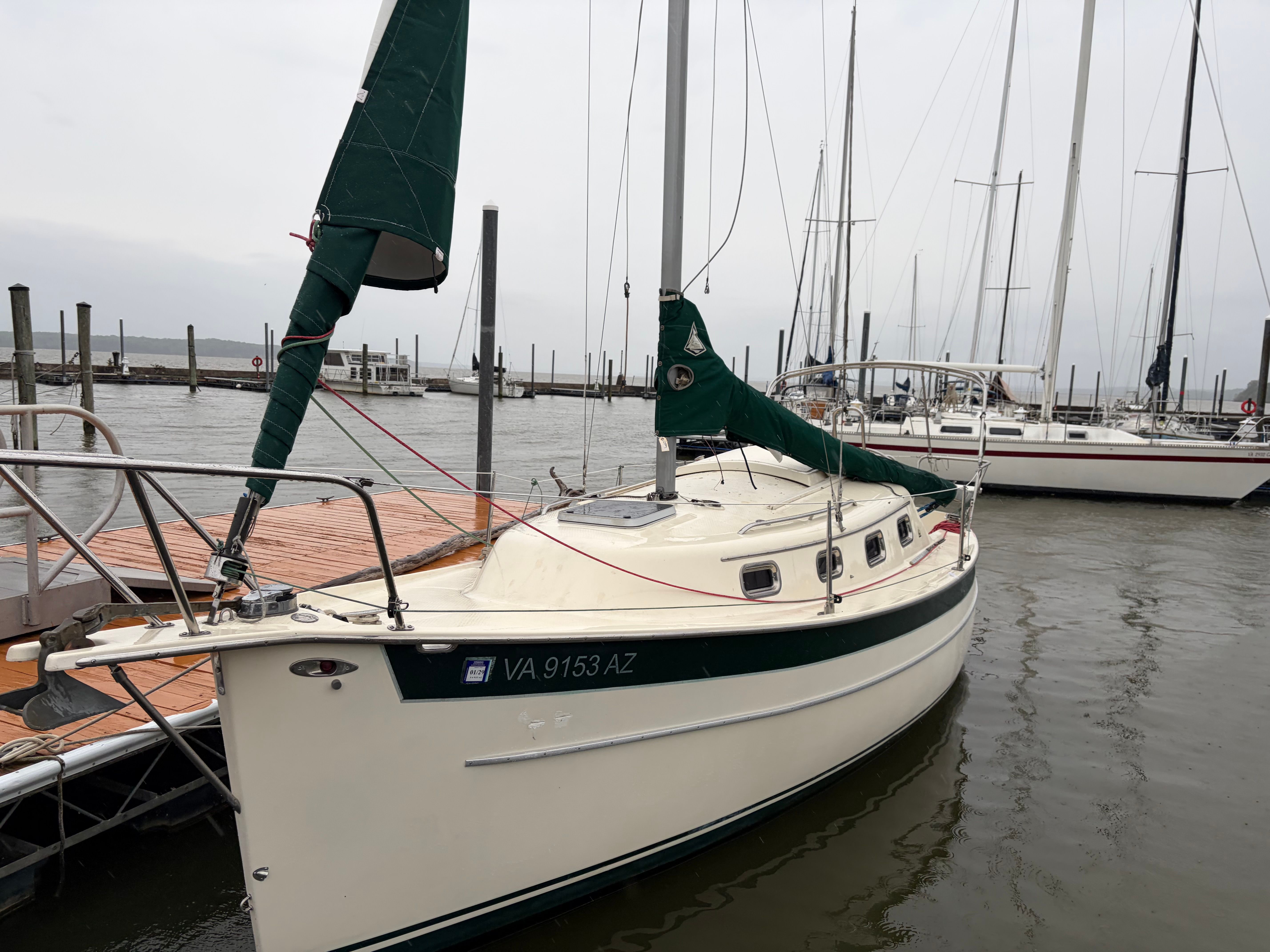 A sailboat docked with green sails, calm water, and other boats in the background.
