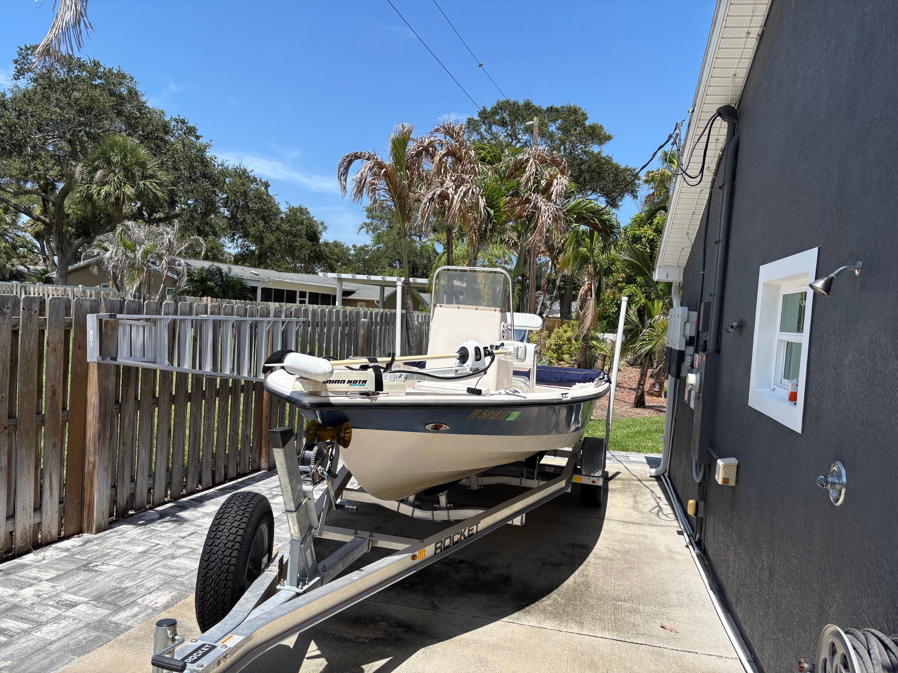 A 2003 Pathfinder 1900T boat on a trailer in a driveway, surrounded by palm trees.