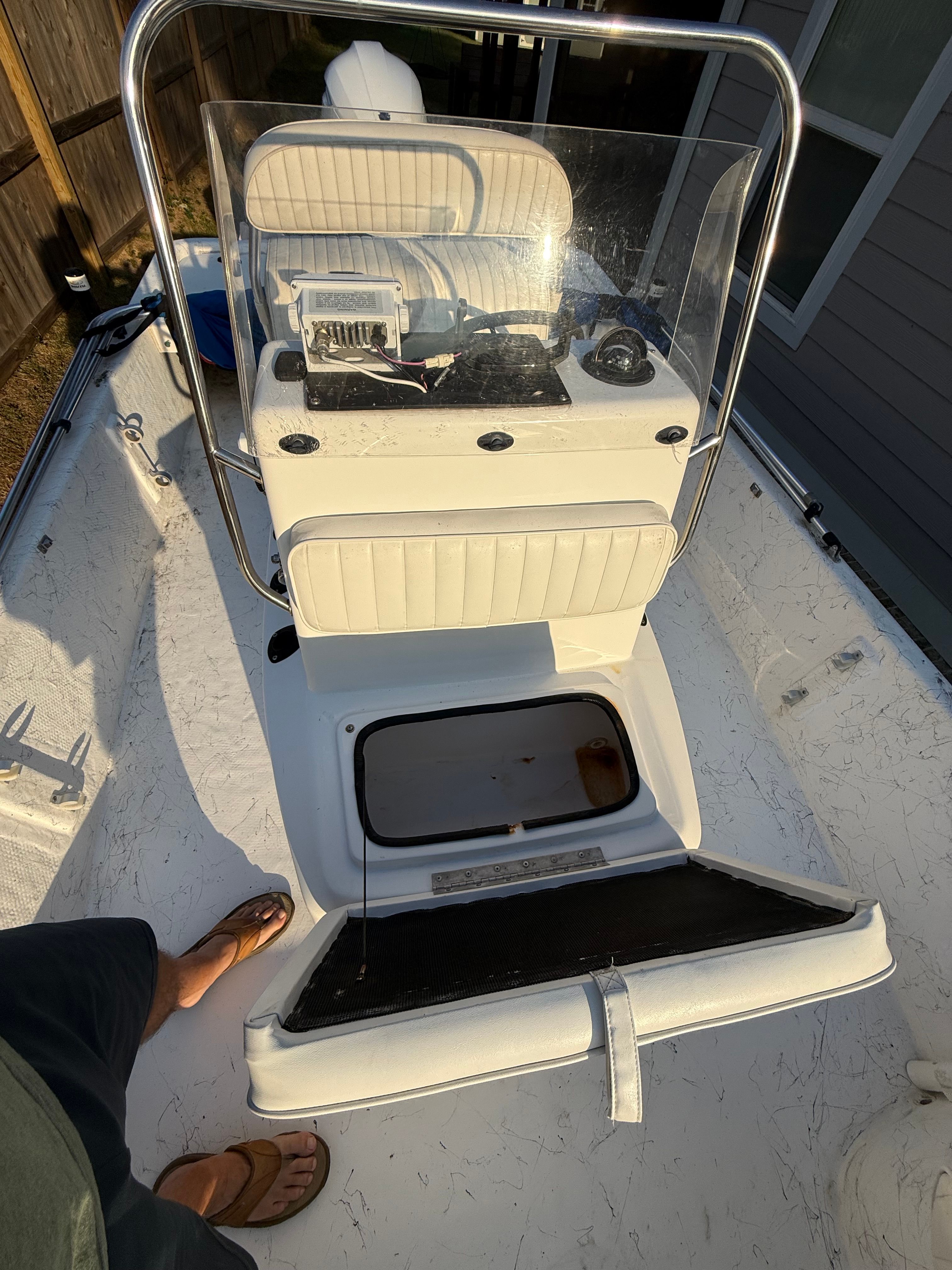 A white boat with a steering console and bench seat, photographed in sunlight.