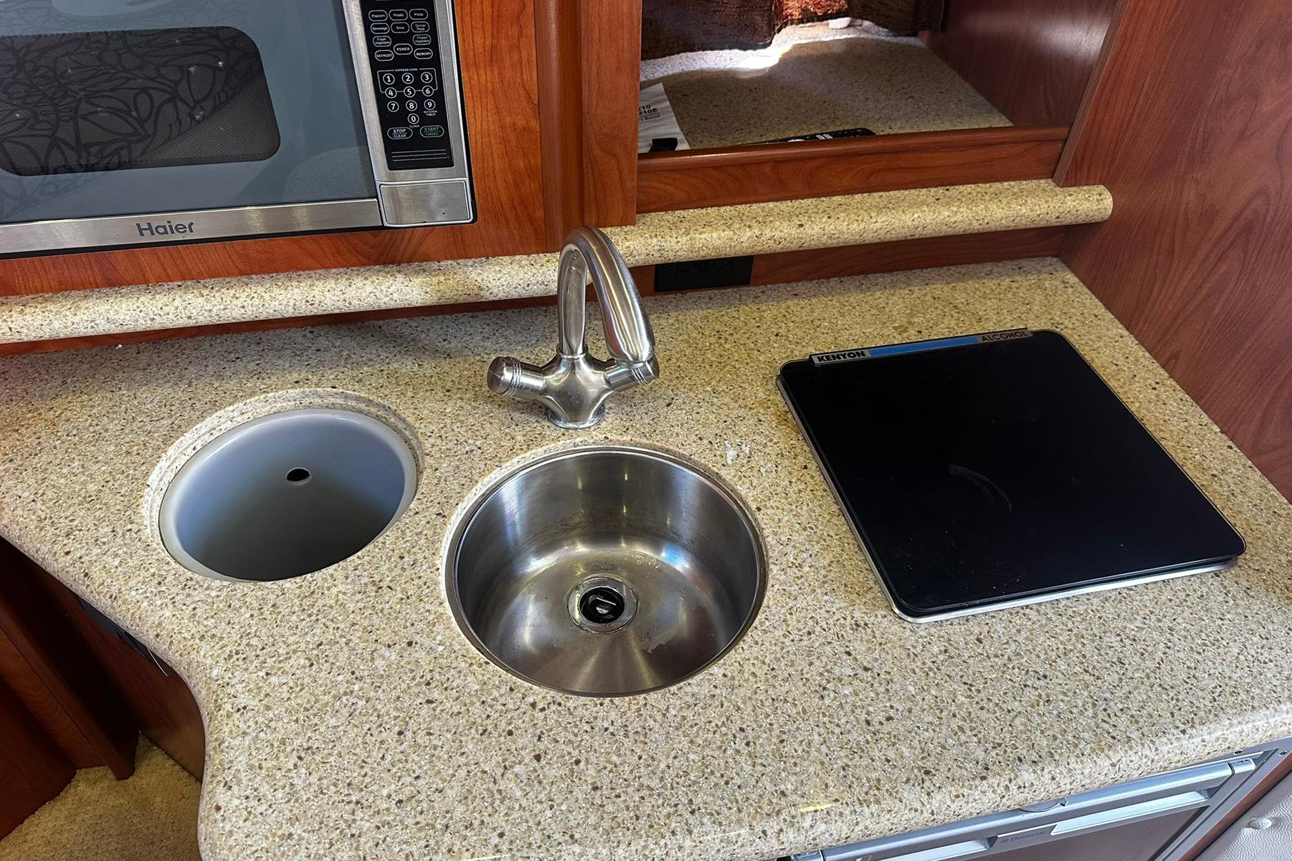 2012 Rinker 310 Express Cruiser LE kitchen with sink, microwave, and cooktop.