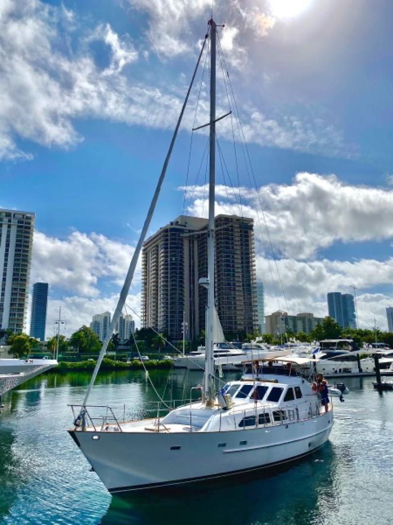 1990 Cheoy Lee Sloop sailing near modern city skyline under blue sky.