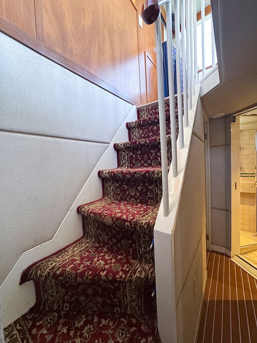 A staircase with patterned carpet leads to an upper deck. Wooden walls and a window are visible.