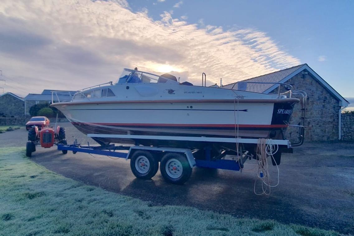 Fairey Spearfish MKIII 1989 boat on trailer, parked near stone building under cloudy sky.