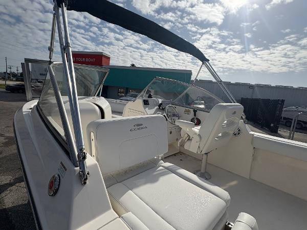 2020 Cobia 220 Dual Console boat with seating, steering wheel, and canopy under a sunny sky.
