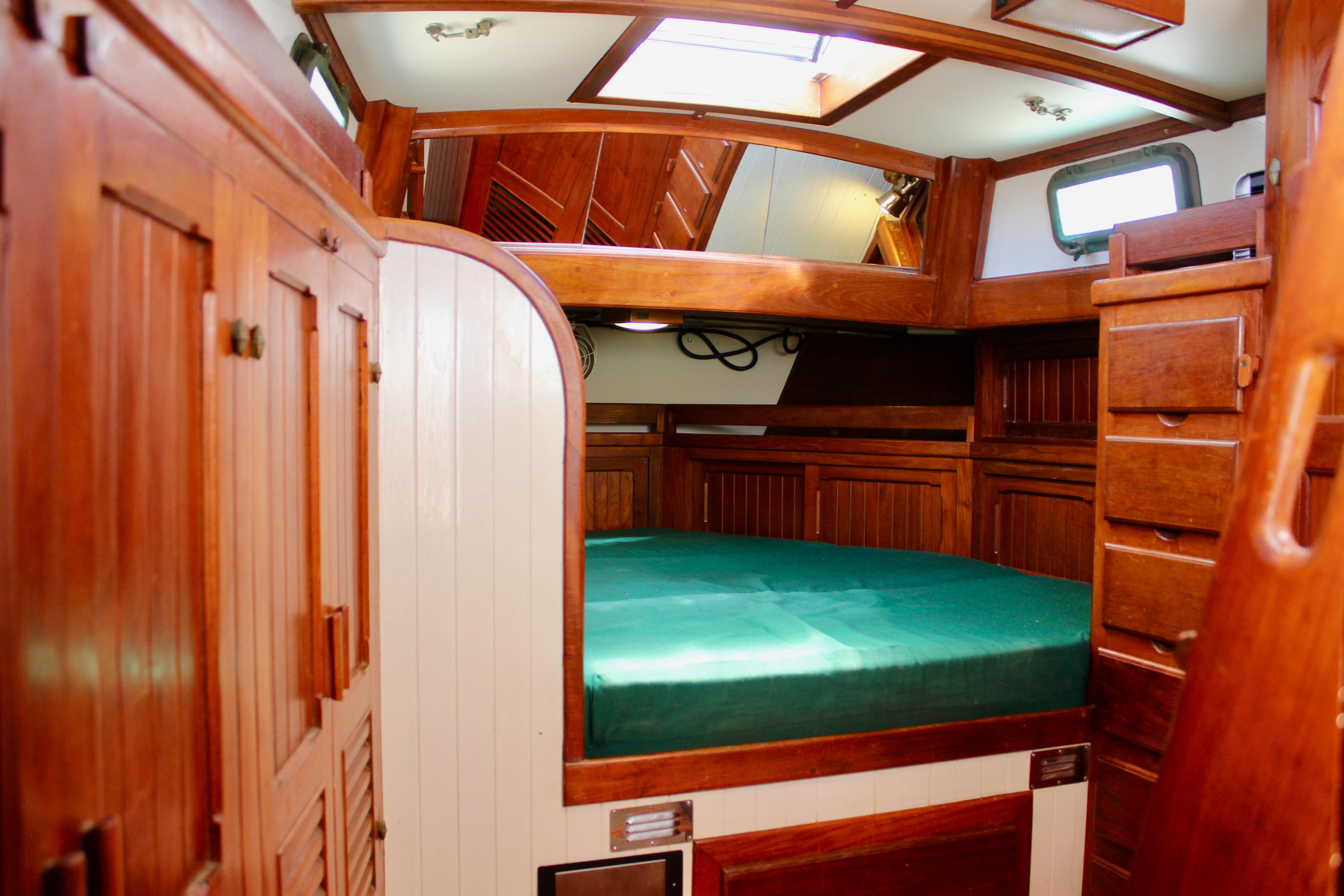 Interior of 1981 Kelly Peterson 46 sailboat with wooden cabinetry and green mattress.