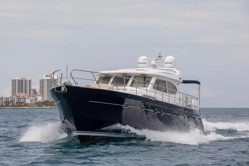 A sleek motor yacht cruising on the sea, with buildings in the background.