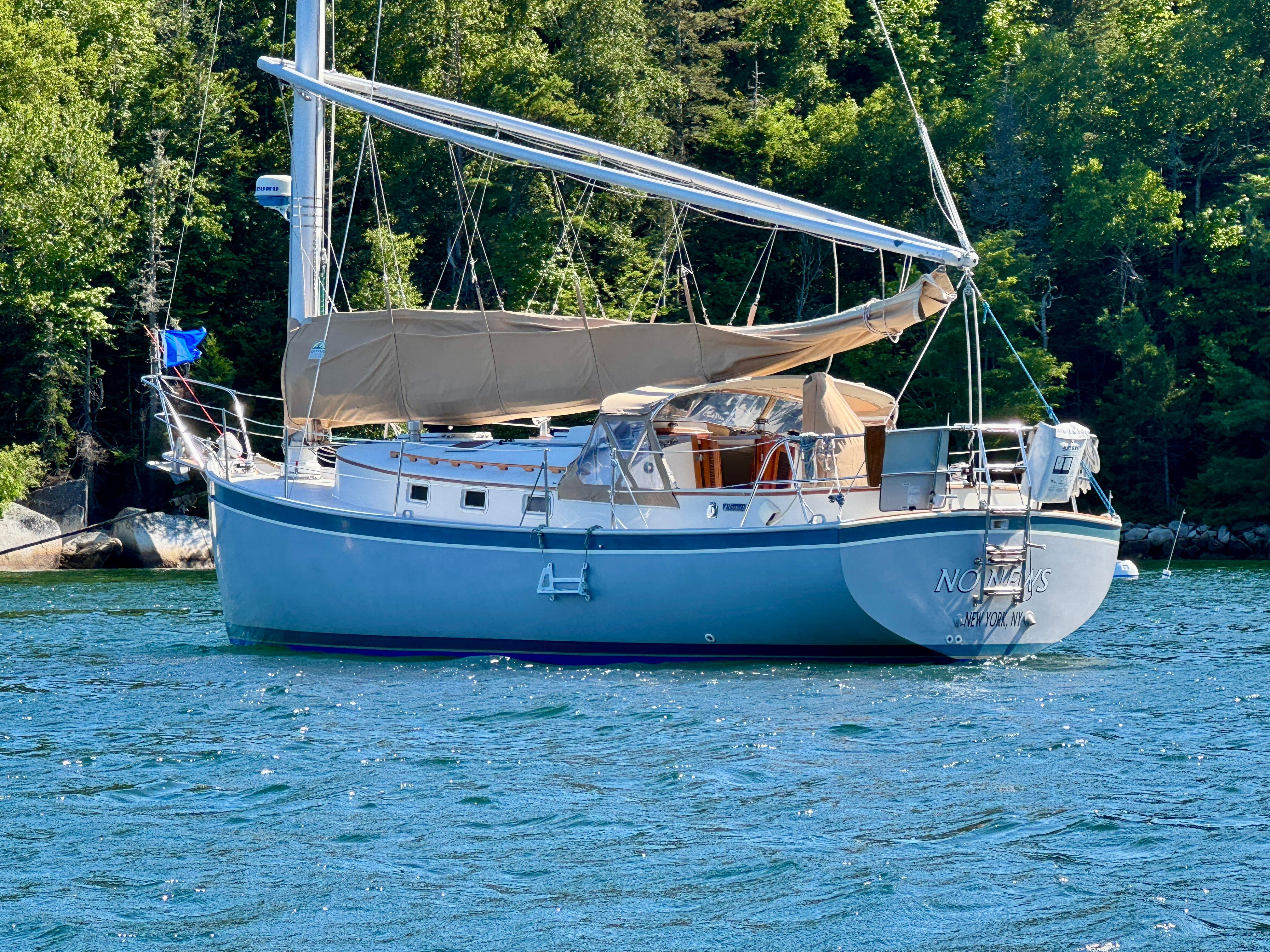 1989 Nonsuch 30 Ultra sailboat anchored on a serene lake with lush green trees.