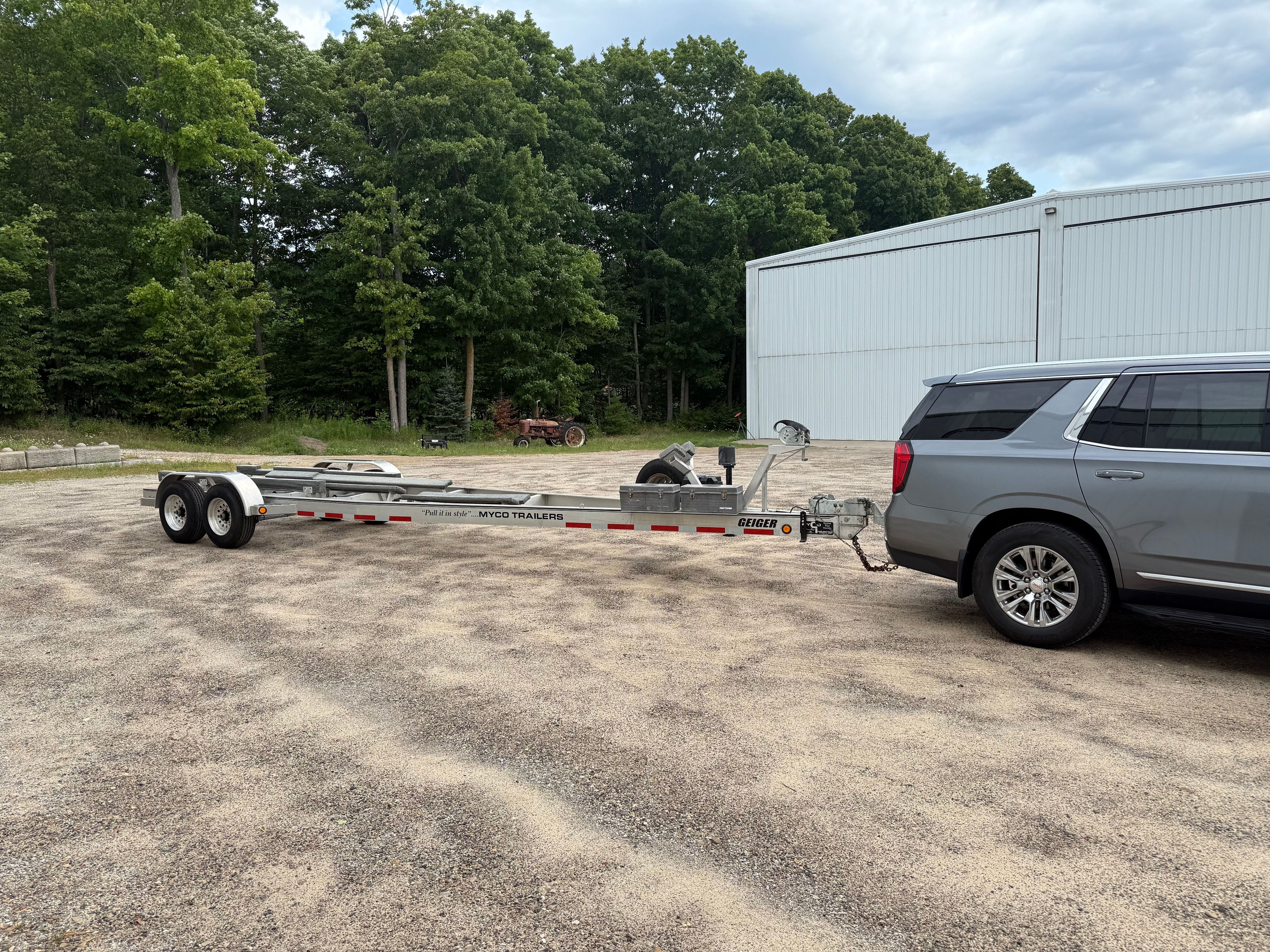 Car with trailer on gravel lot in front of warehouse.