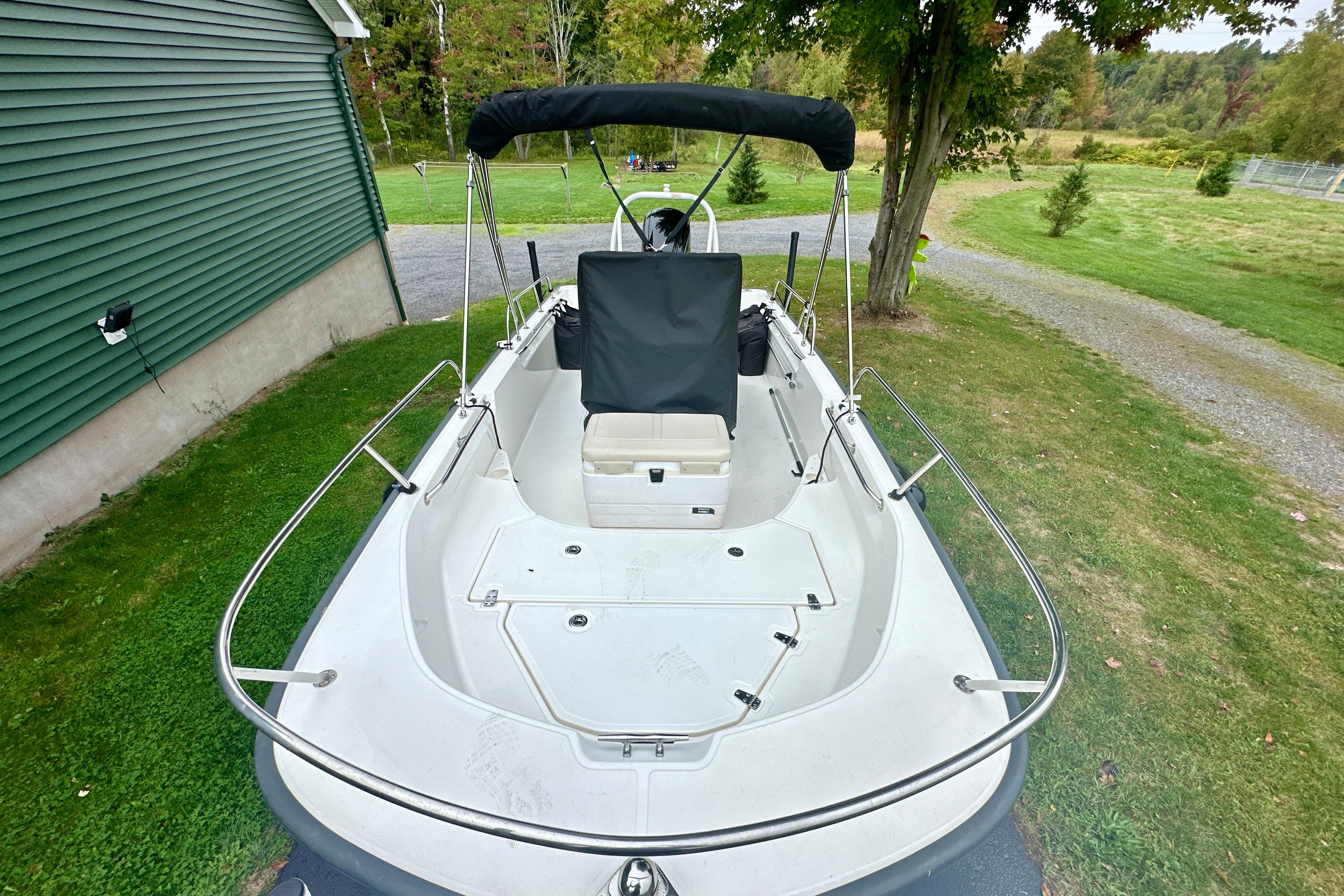 2024 Boston Whaler 170 Montauk boat with canopy, parked on grass near a green building.