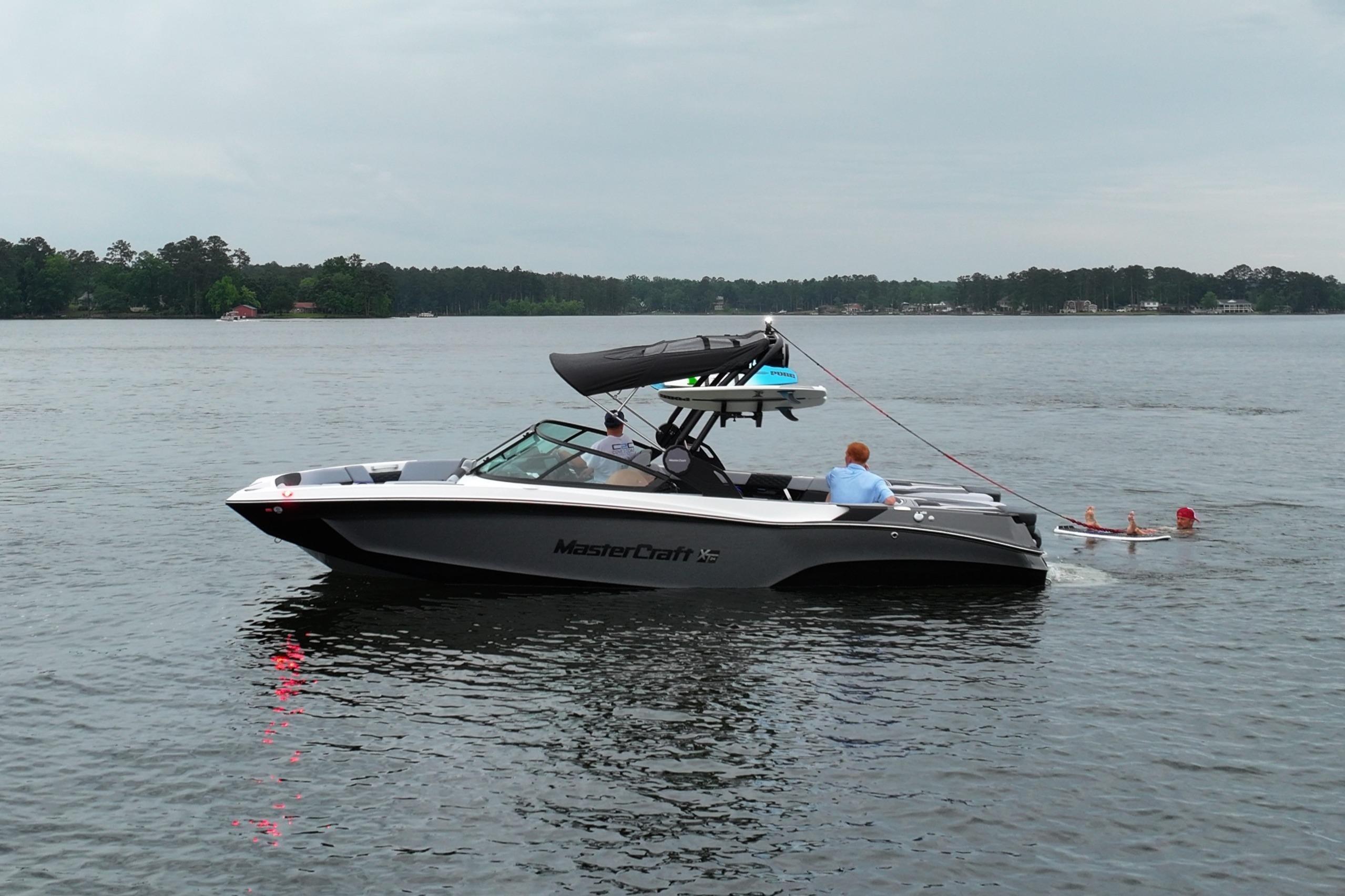 2025 MasterCraft XT24 boat on a lake with people wakeboarding.