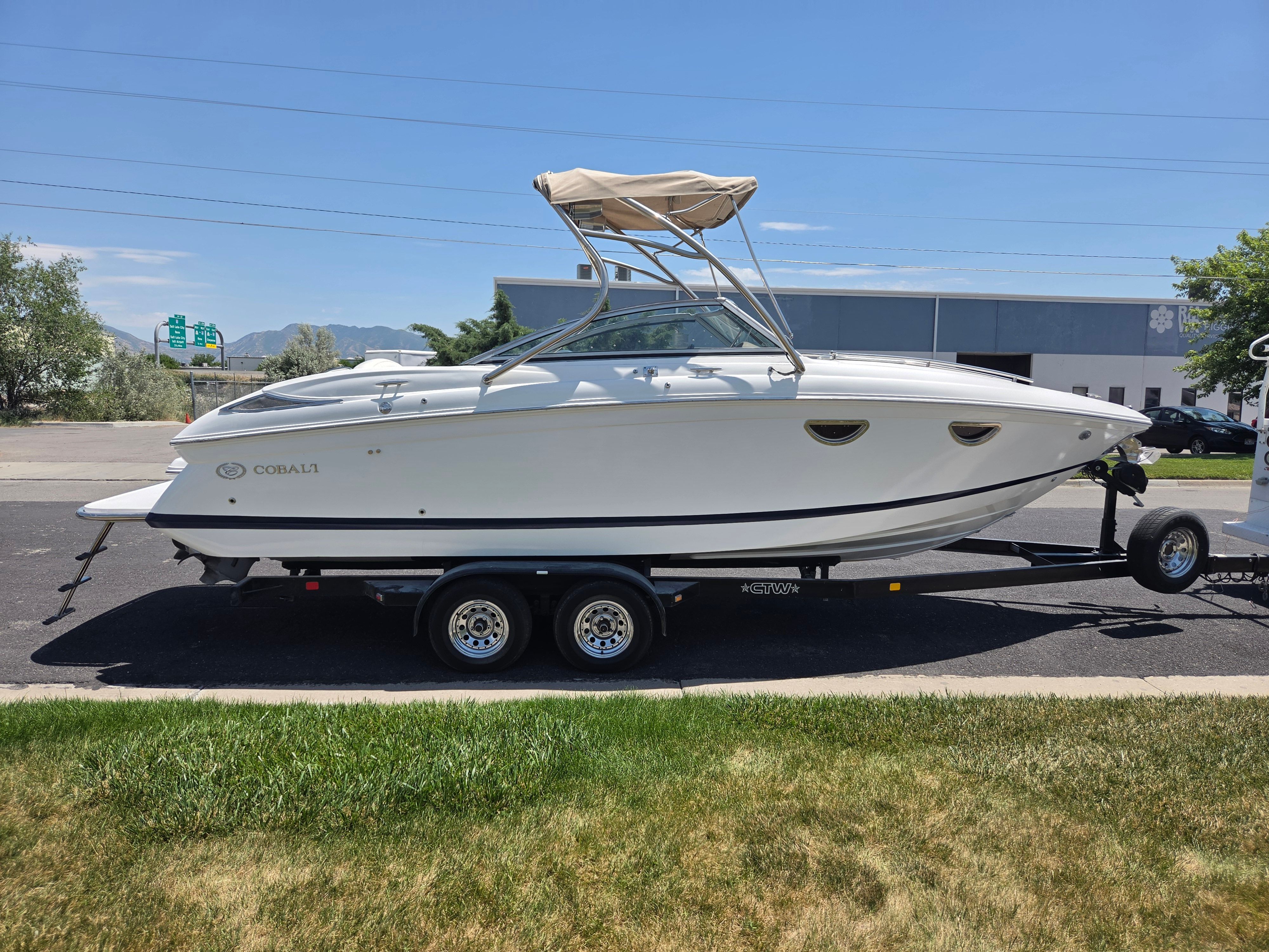 A white Cobalt 243 boat on a trailer, parked on a street in sunny weather.
