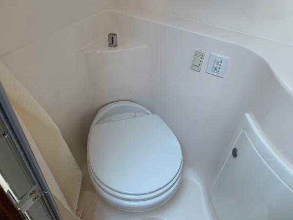 The image shows a compact boat toilet with white walls and a small sink.