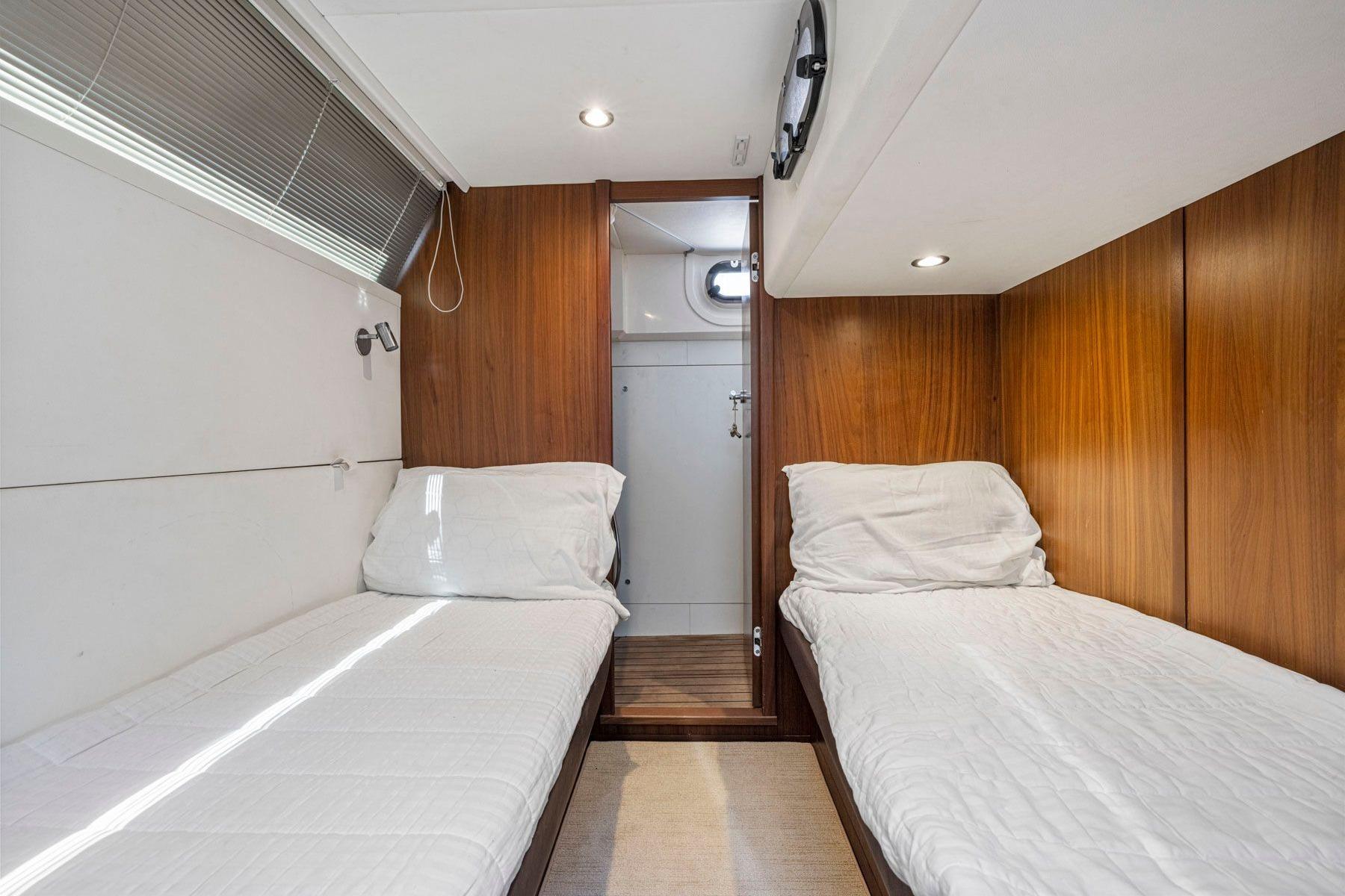 Twin cabin interior of 2015 Princess 60 Flybridge Motor Yacht, featuring wood paneling and cozy beds.