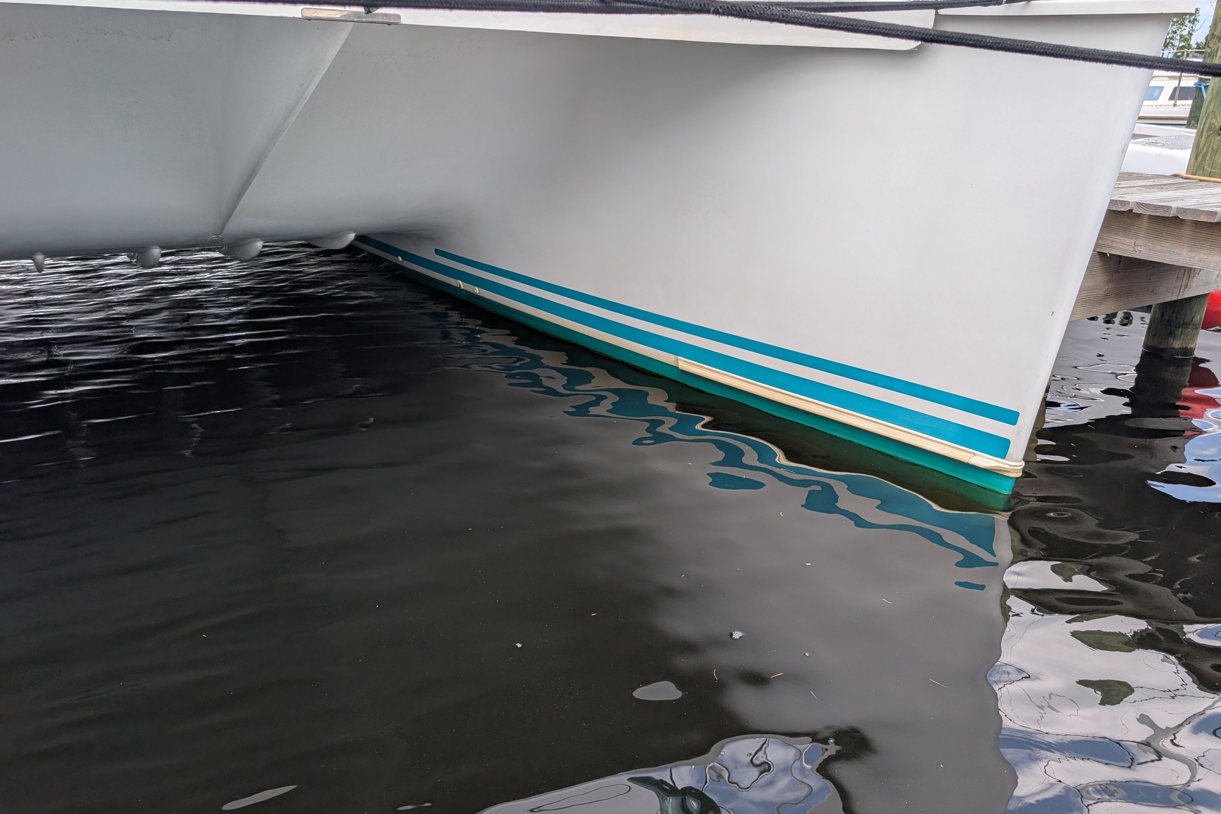 2004 PDQ 34 Powercat boat hull with blue stripes, docked in calm water.