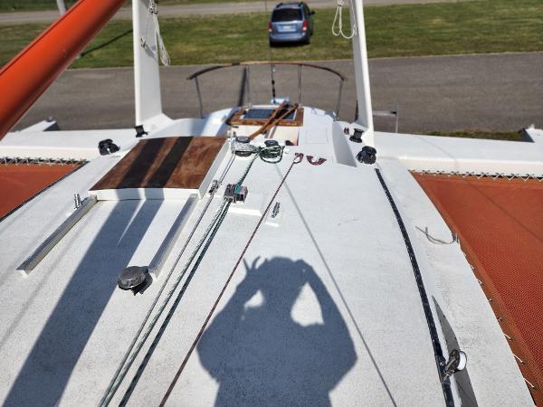 1985 Crowther Buccaneer sailboat deck with rigging and shadow, parked car in background.