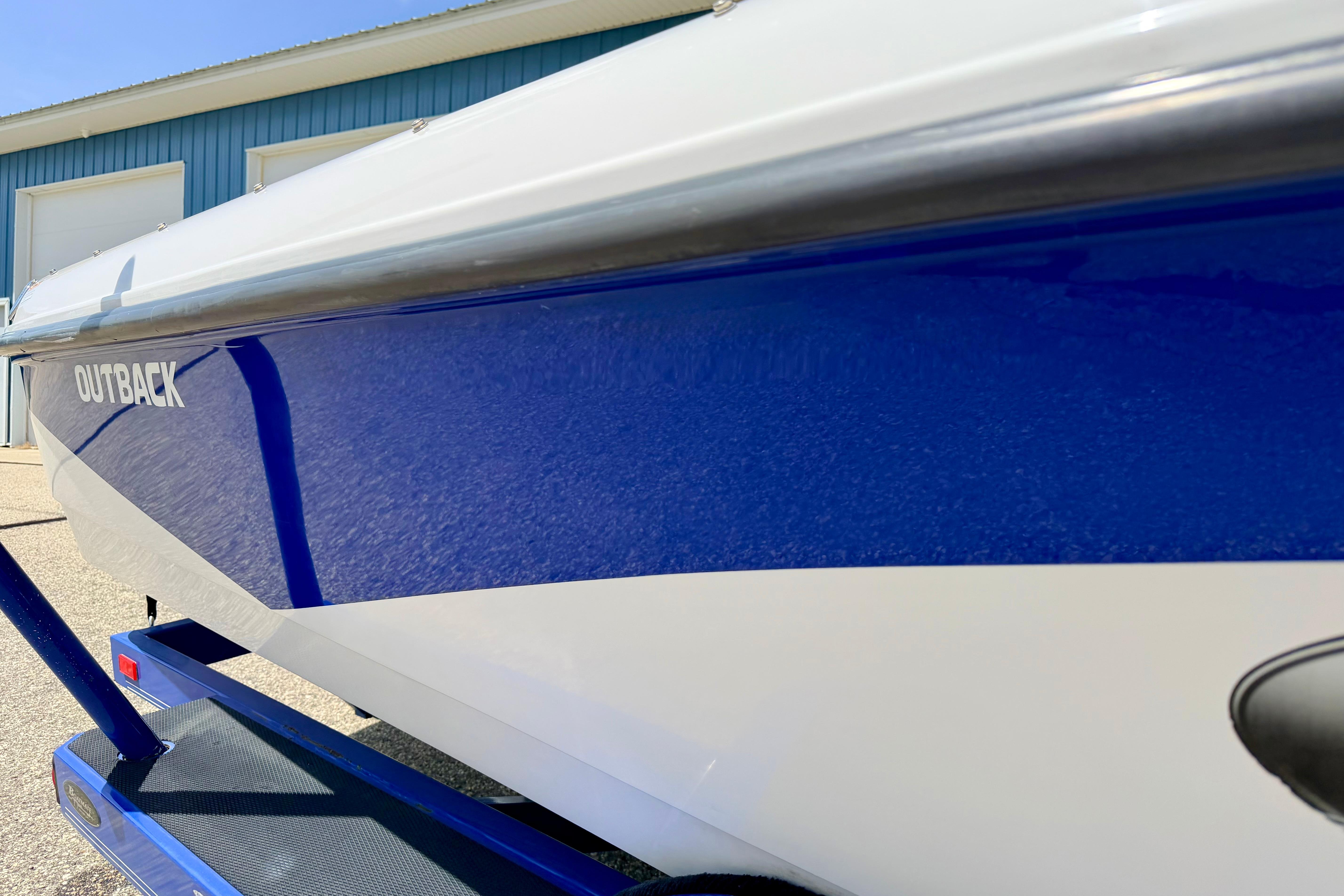 2008 Moomba Outback V boat with blue and white exterior, parked near a blue building.