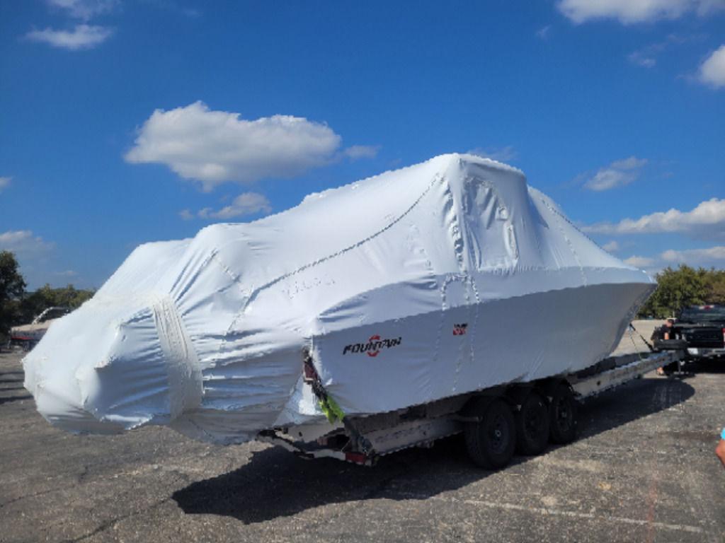 2024 Fountain 38 SCX boat covered in protective wrap on a trailer under a blue sky.
