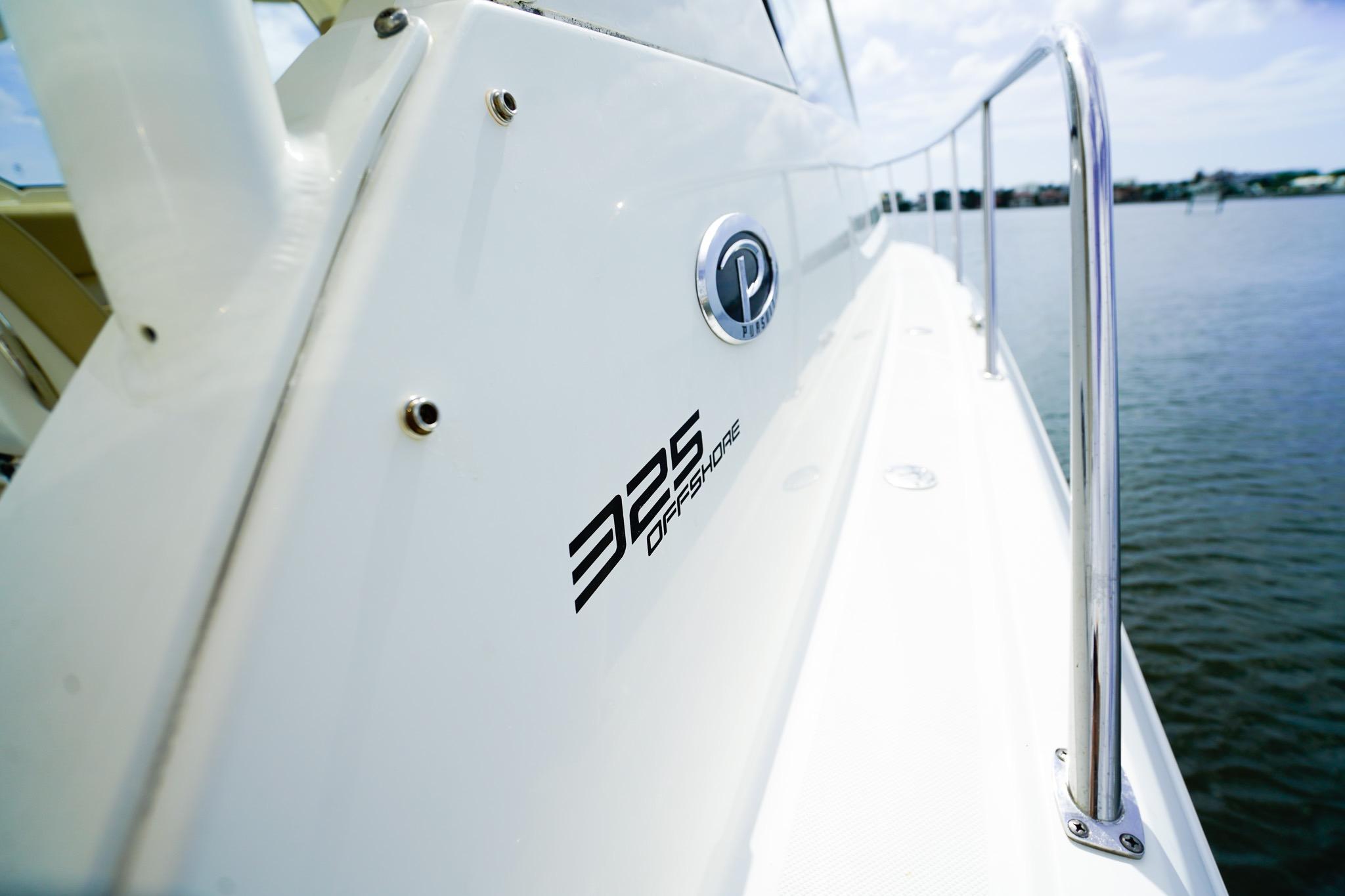 2020 Pursuit OS 325 Offshore boat side view with logo, railing, and water backdrop.