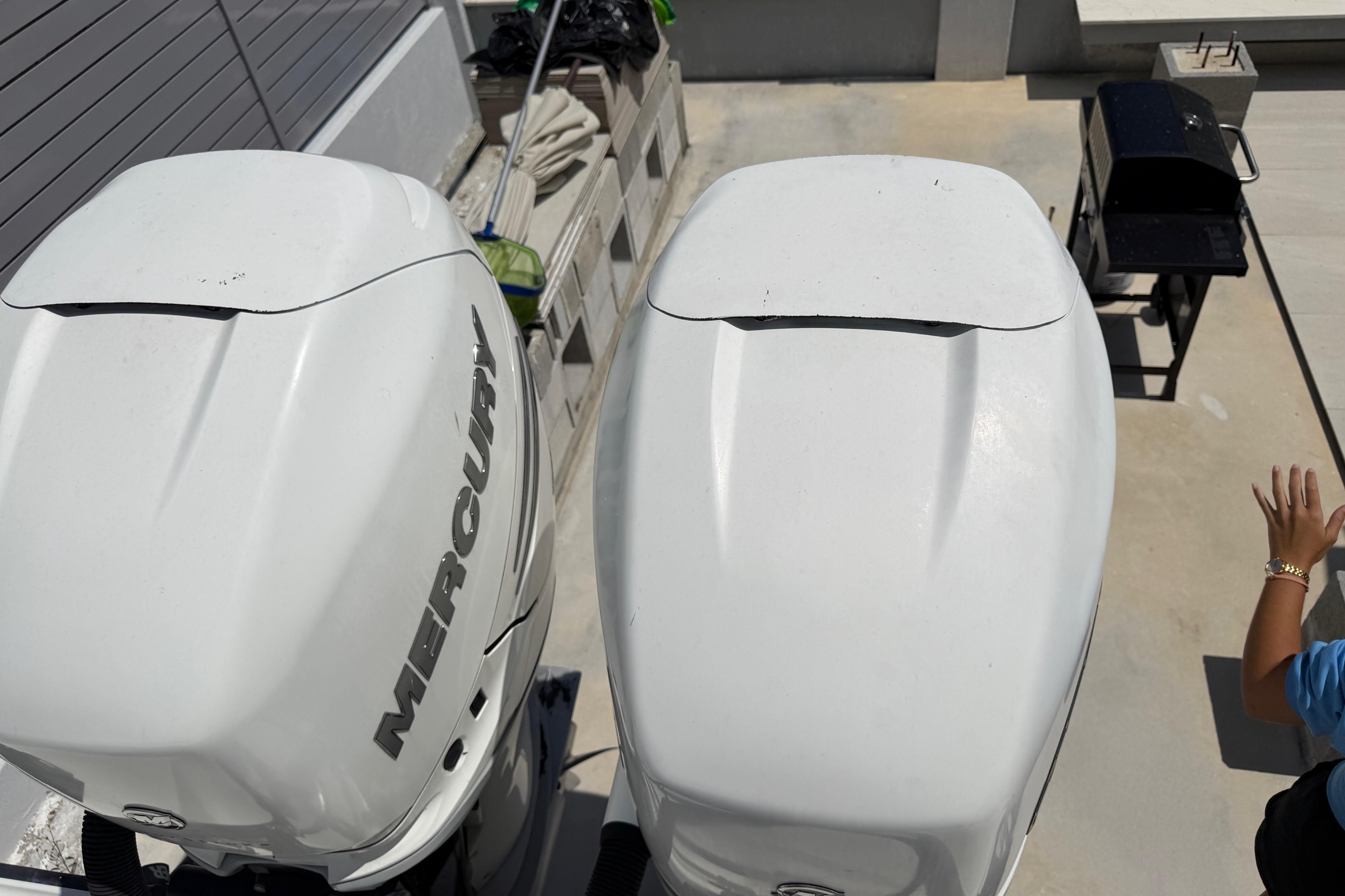 Two large outboard motors on a boat, with a grill in the background.