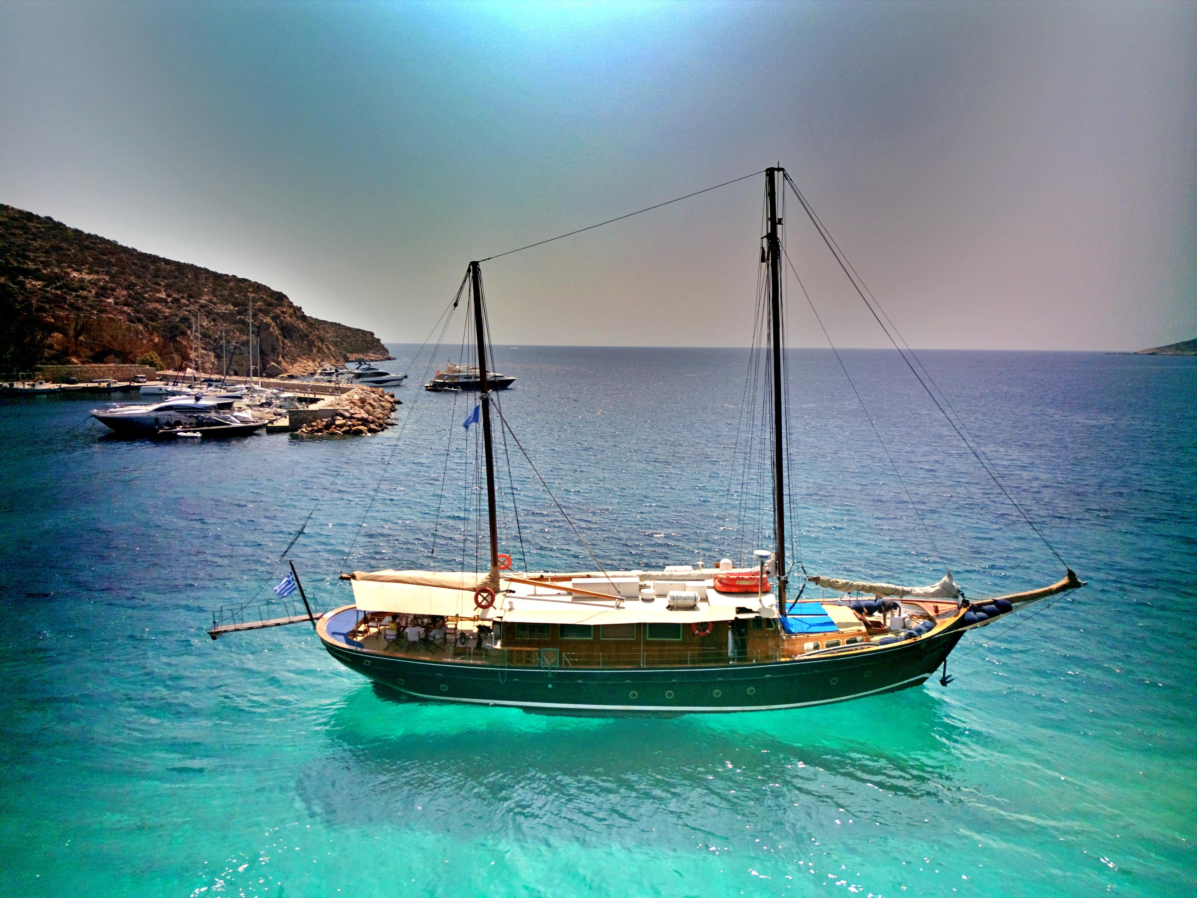 Vintage 1969 Psarros Shipyard sailboat on turquoise waters near rocky coastline.