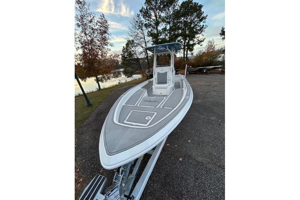 2025 Mako 24 APEX boat on trailer by lakeside, surrounded by autumn trees.